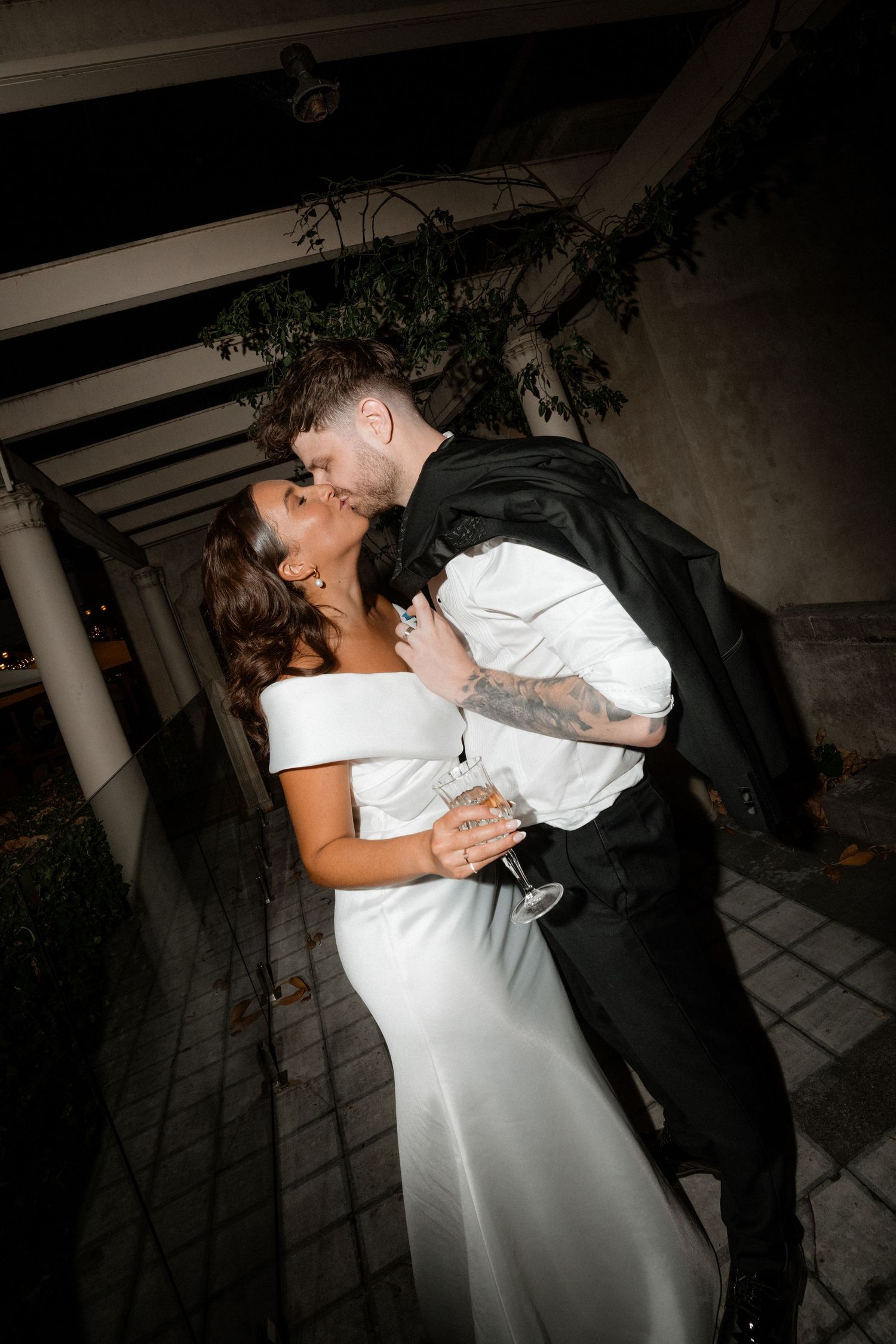 A dramatic nighttime dip kiss between newlyweds under a covered outdoor venue with romantic lighting.