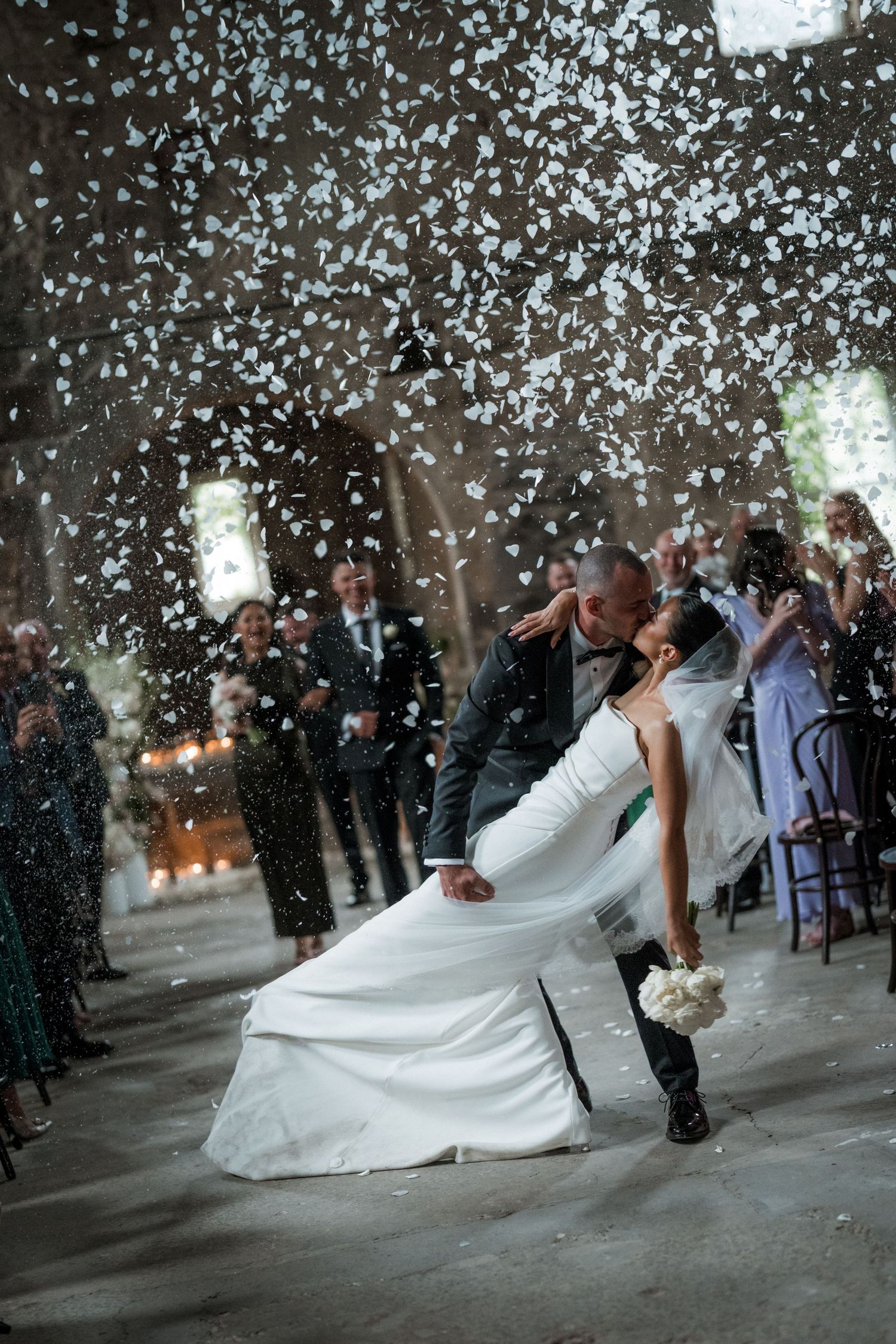 Romantic dance dip with confetti falling in atmospheric wedding venue.