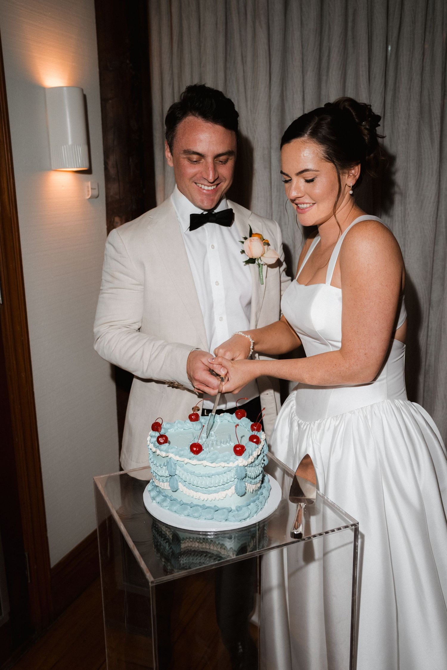 Couple cuts into a light blue wedding cake decorated with delicate details.