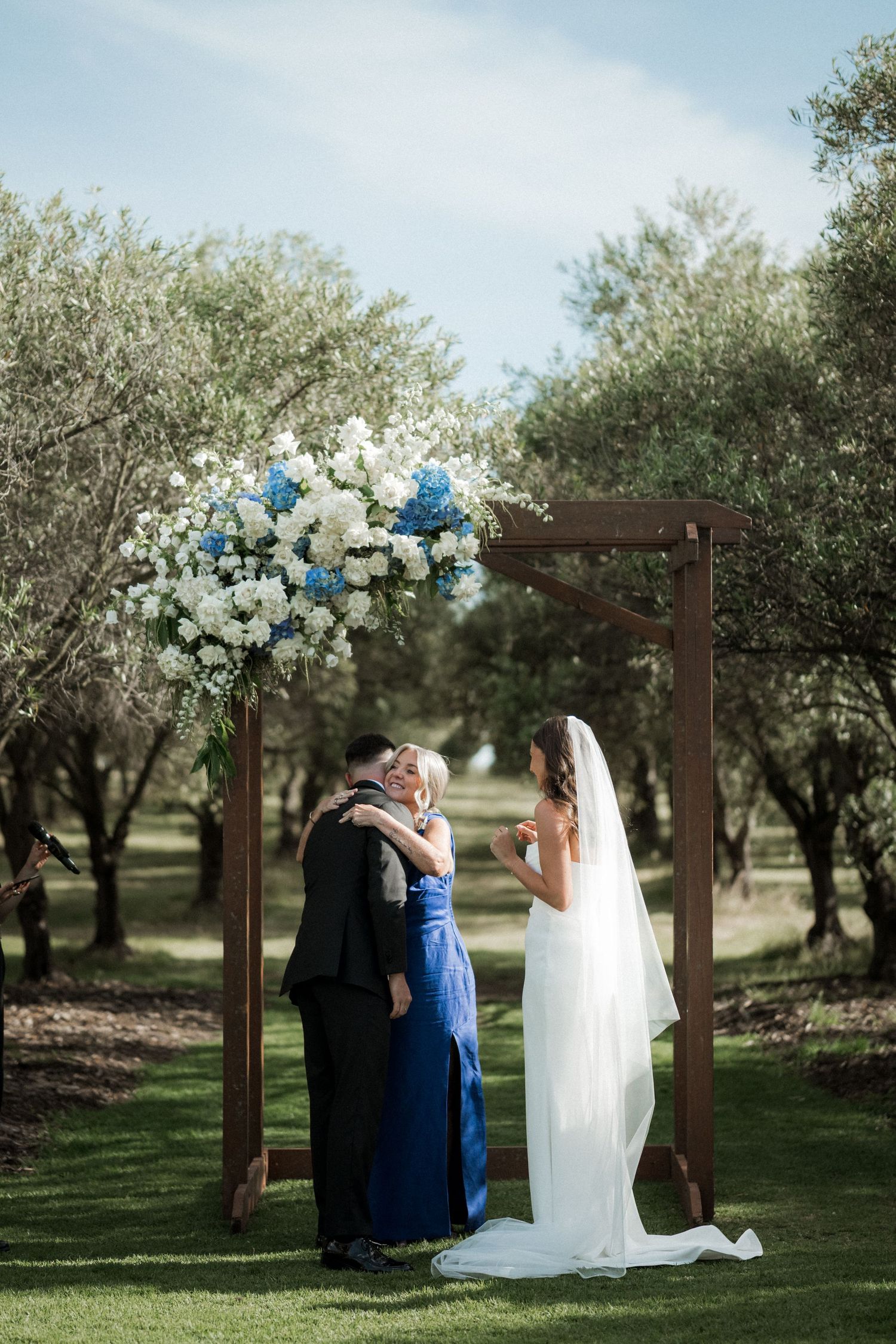 Wedding couple shares an intimate moment in a serene olive grove under wooden archway.