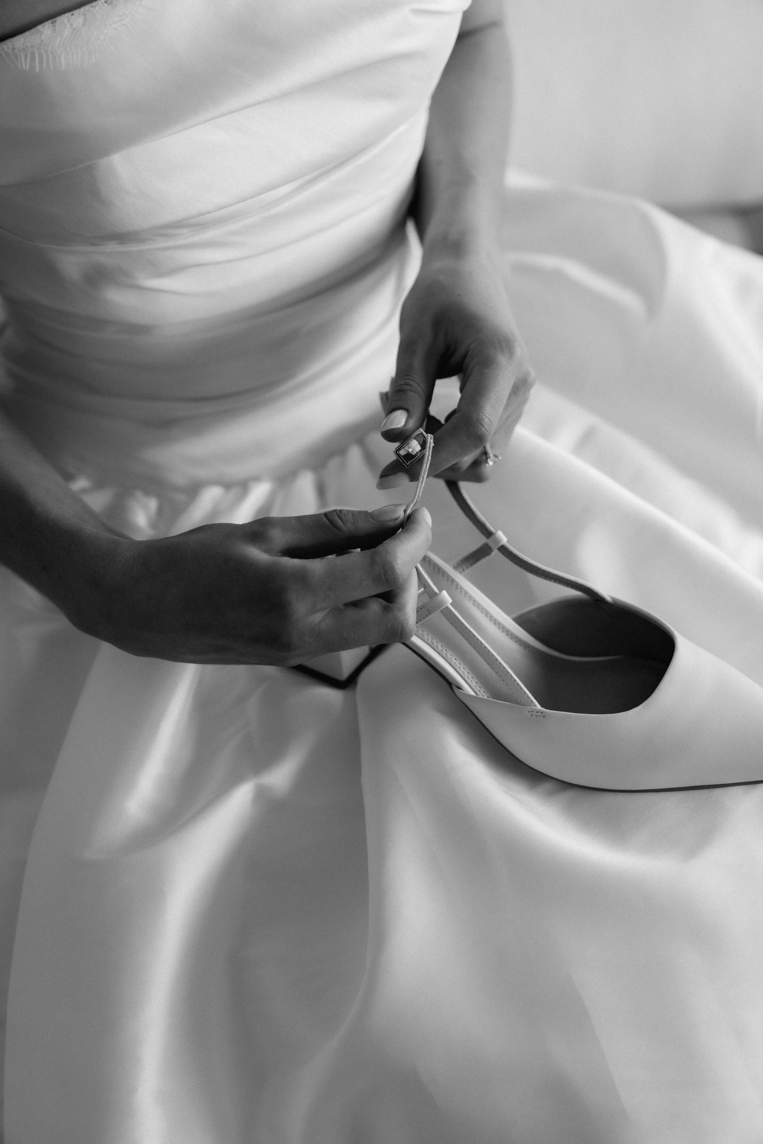 Close-up of white bridal shoes being put on against flowing wedding dress fabric.