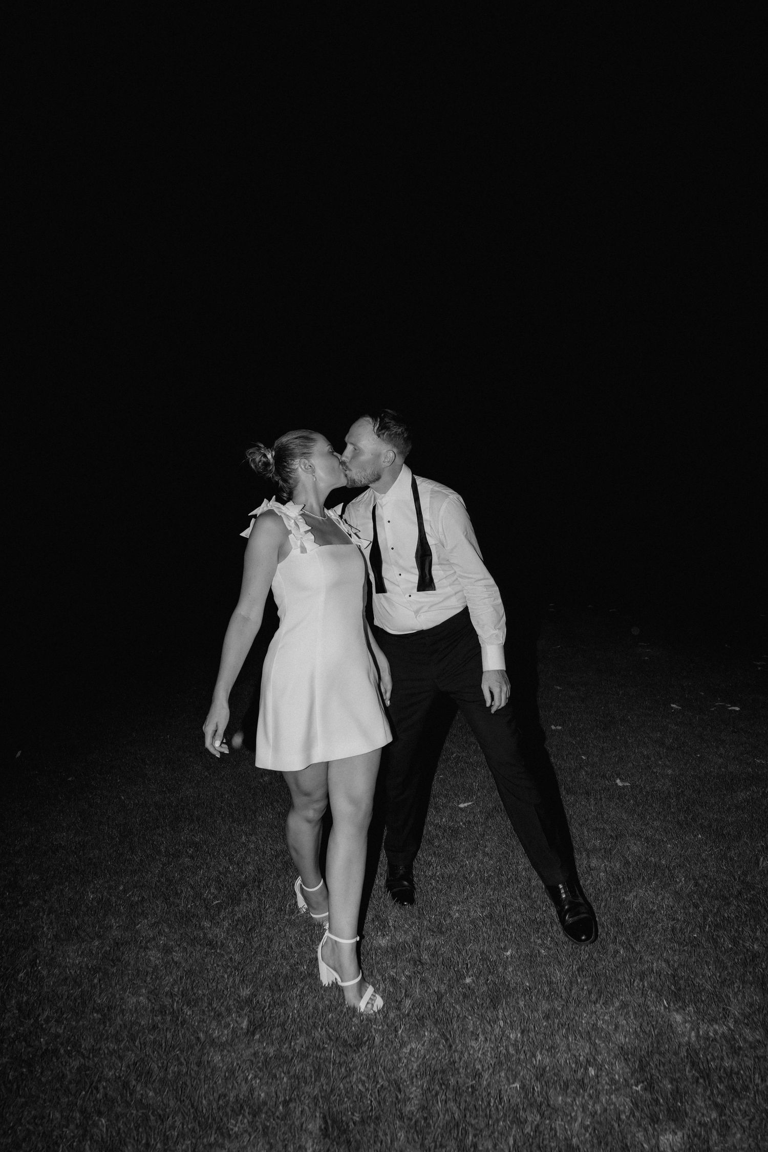 A black and white nighttime photo showing dancers' feet and legs on grass.