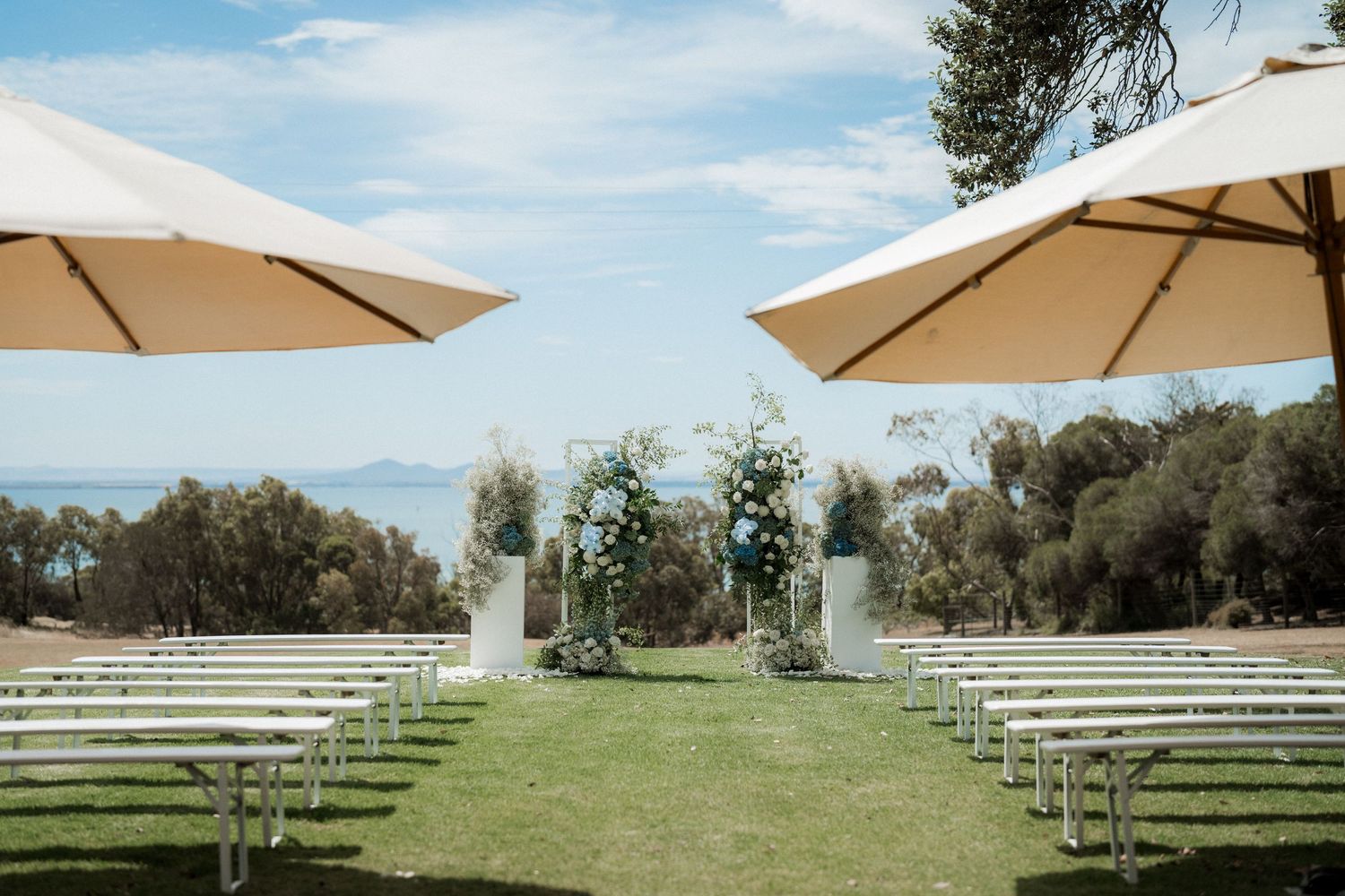 White umbrellas and chairs set up in rows on a grassy outdoor venue with mountains in the background.