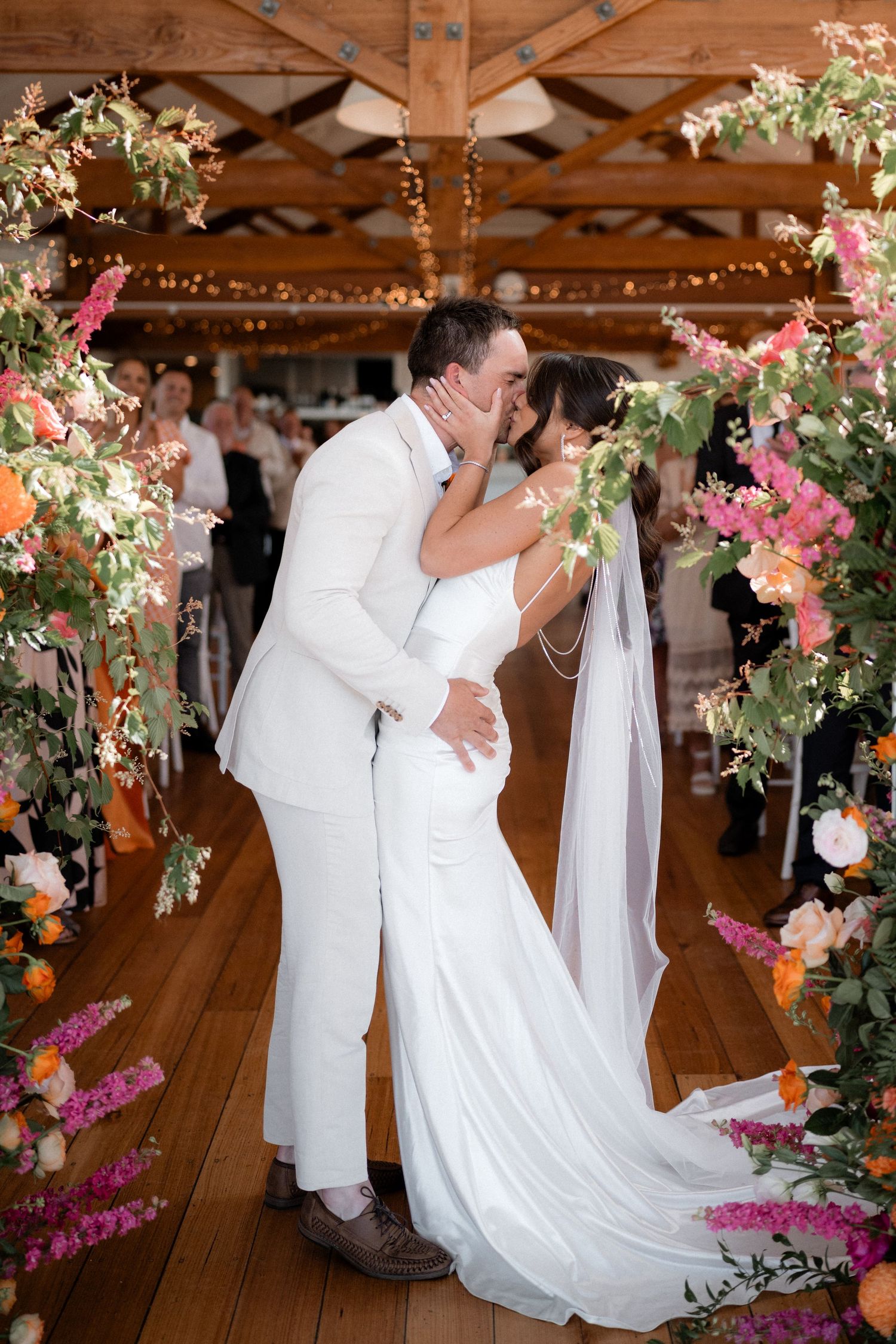 Wedding couple sharing first dance under rustic wooden beams decorated with pink floral arrangements.