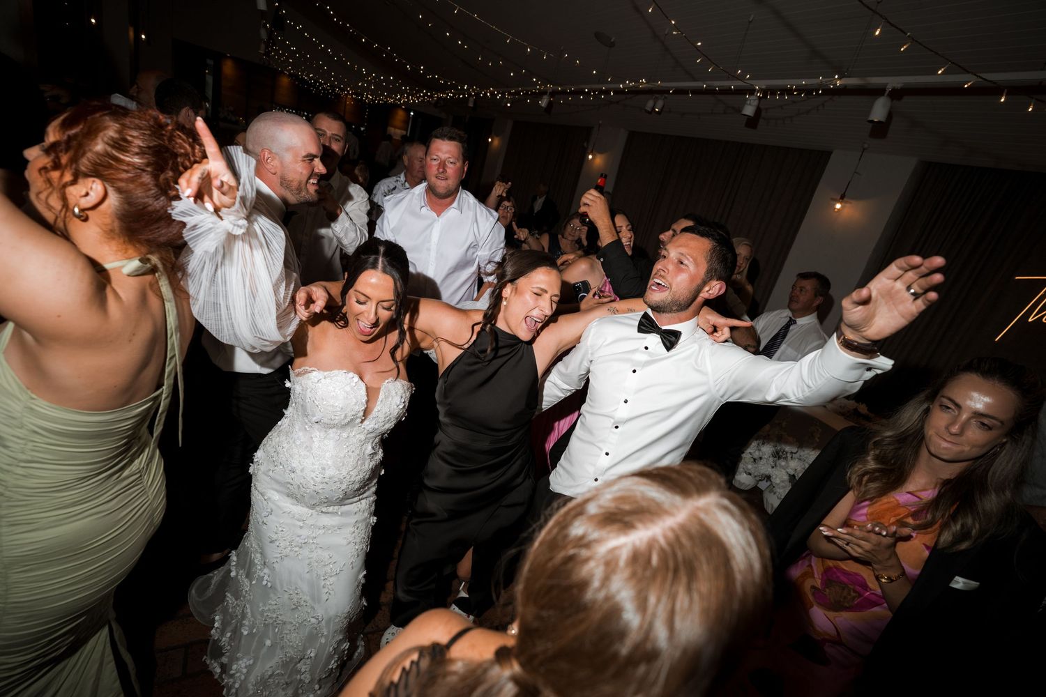 Wedding reception dance party with string lights and guests celebrating on the dance floor.