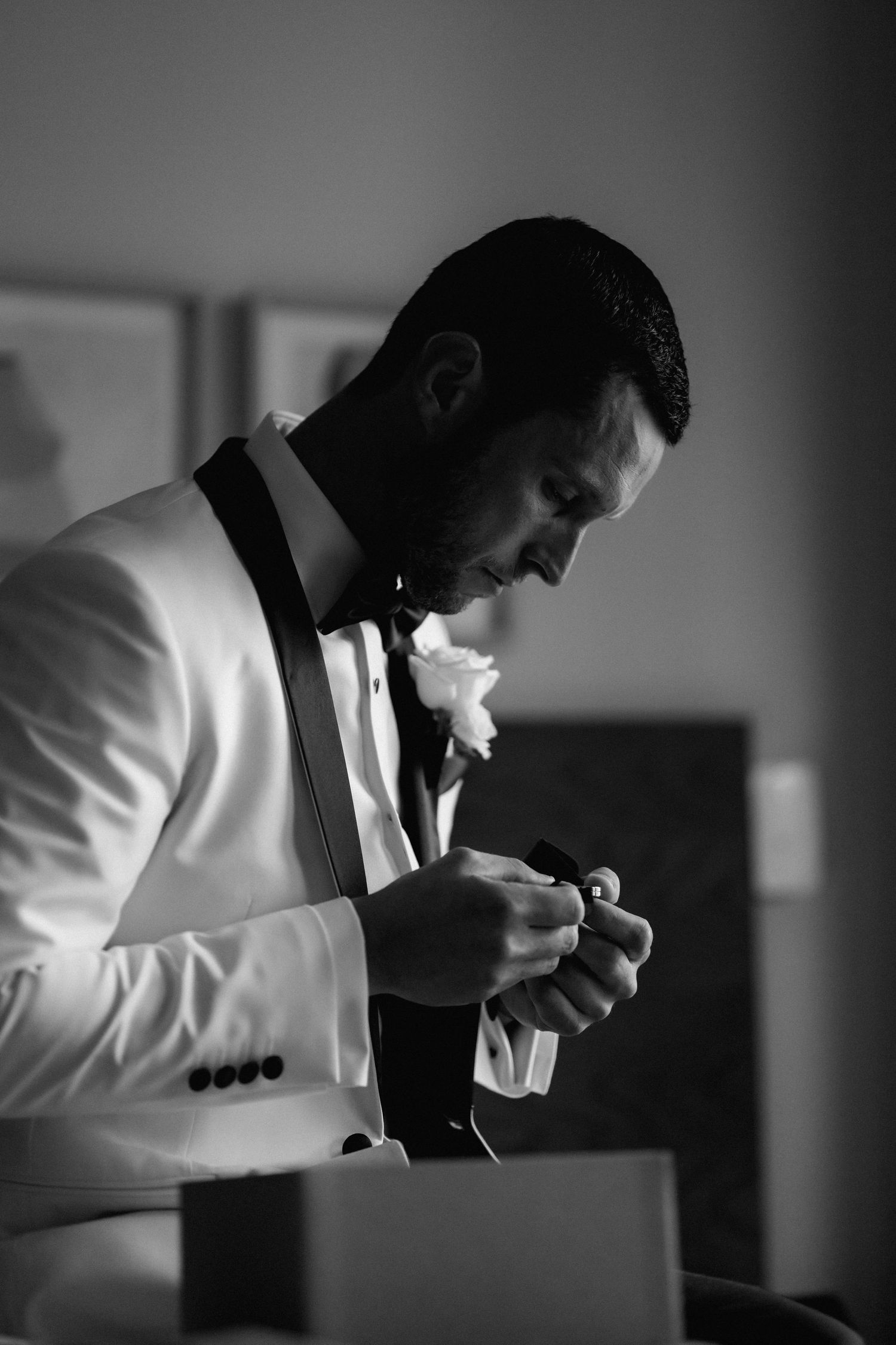 Silhouette of a person in a white suit jacket examining something in dramatic black and white lighting.