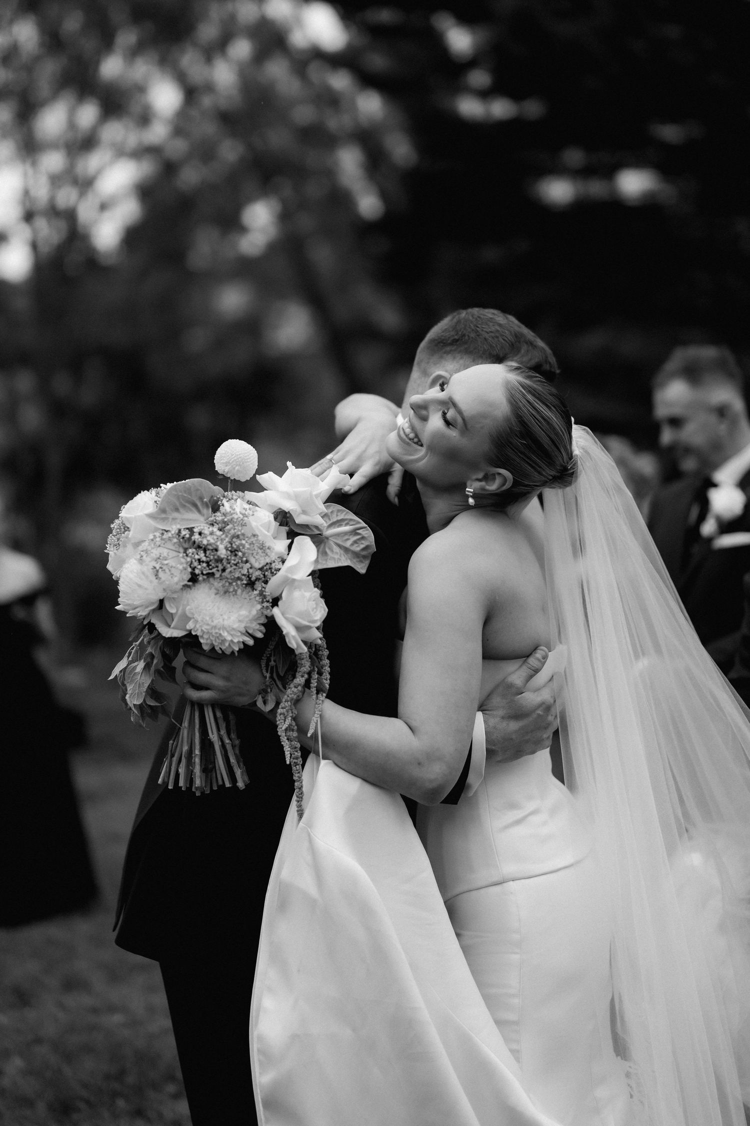 Elegant black and white wedding photo capturing an intimate moment with a bouquet between two attendees.
