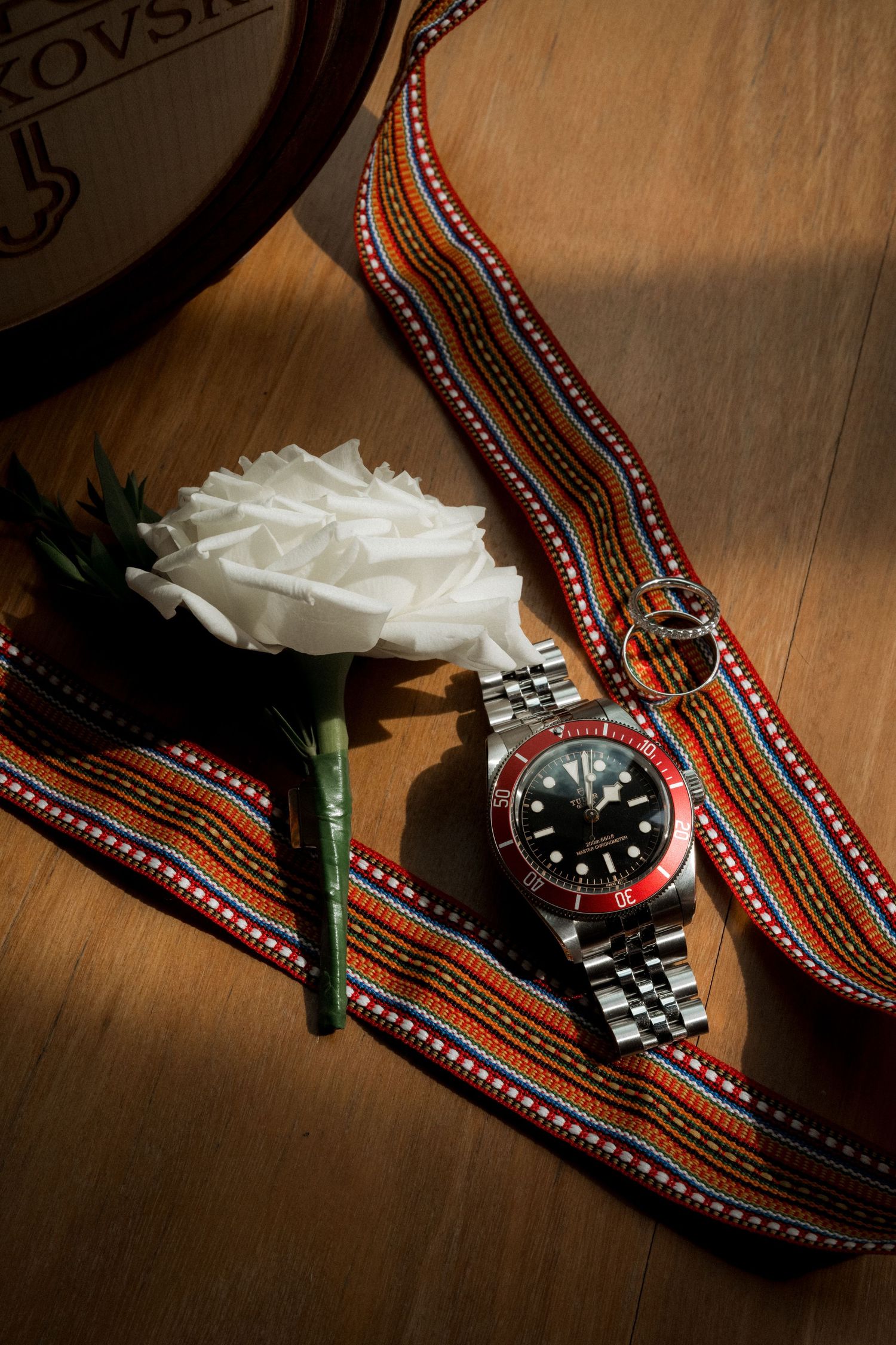 A wristwatch and white boutonniere displayed on a decorative ethnic patterned fabric.