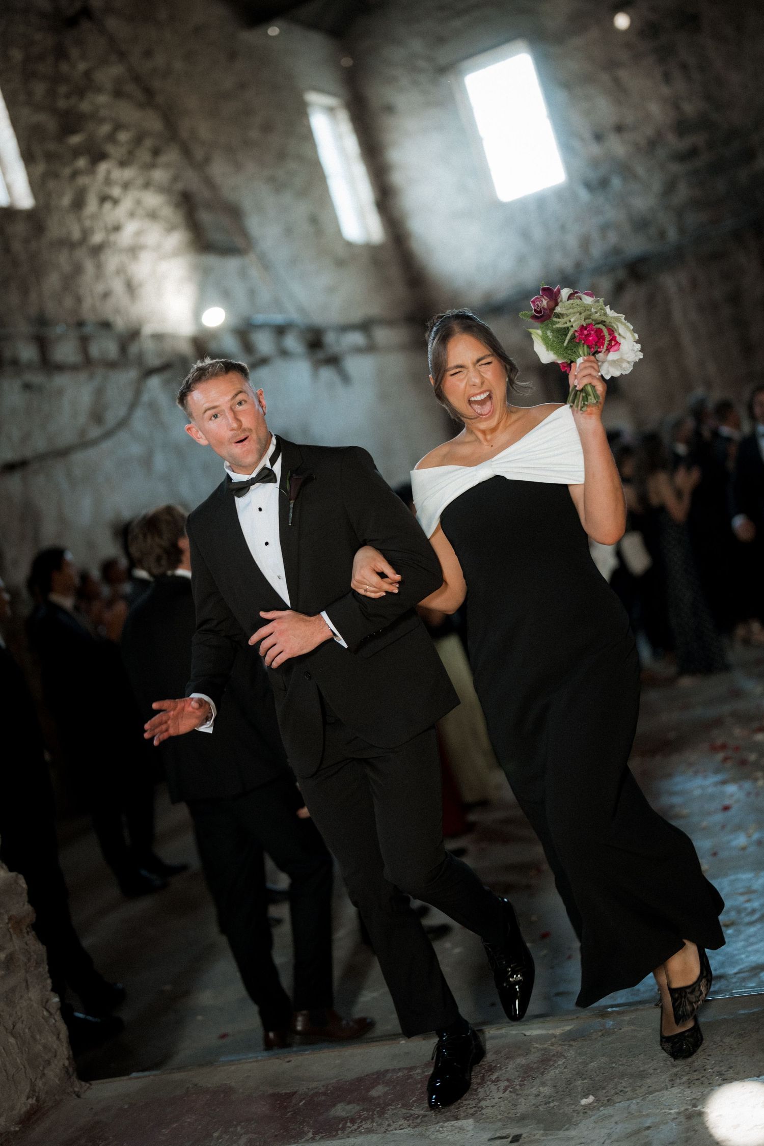 A joyful couple celebrating during their wedding recessional in a rustic stone venue with dramatic lighting.