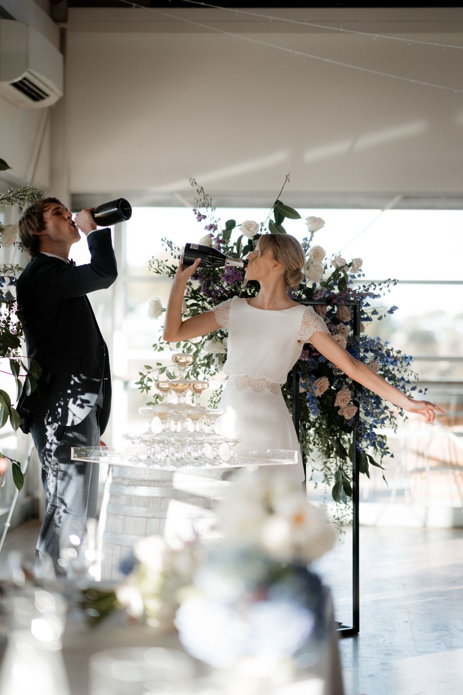 Newlyweds share a celebratory champagne toast against a floral backdrop at their reception.