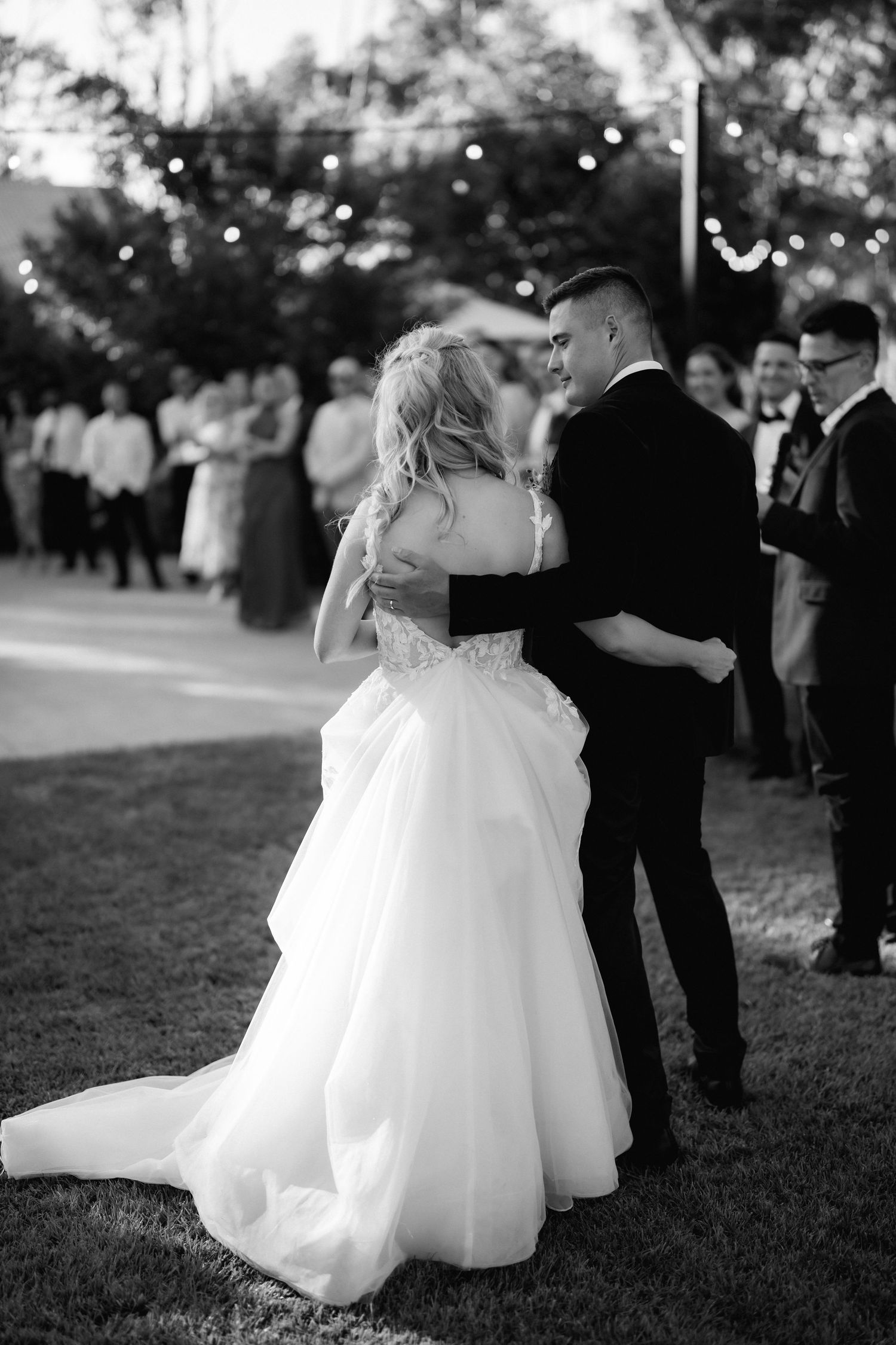 Bride and groom share their first dance under evening lights at outdoor reception.