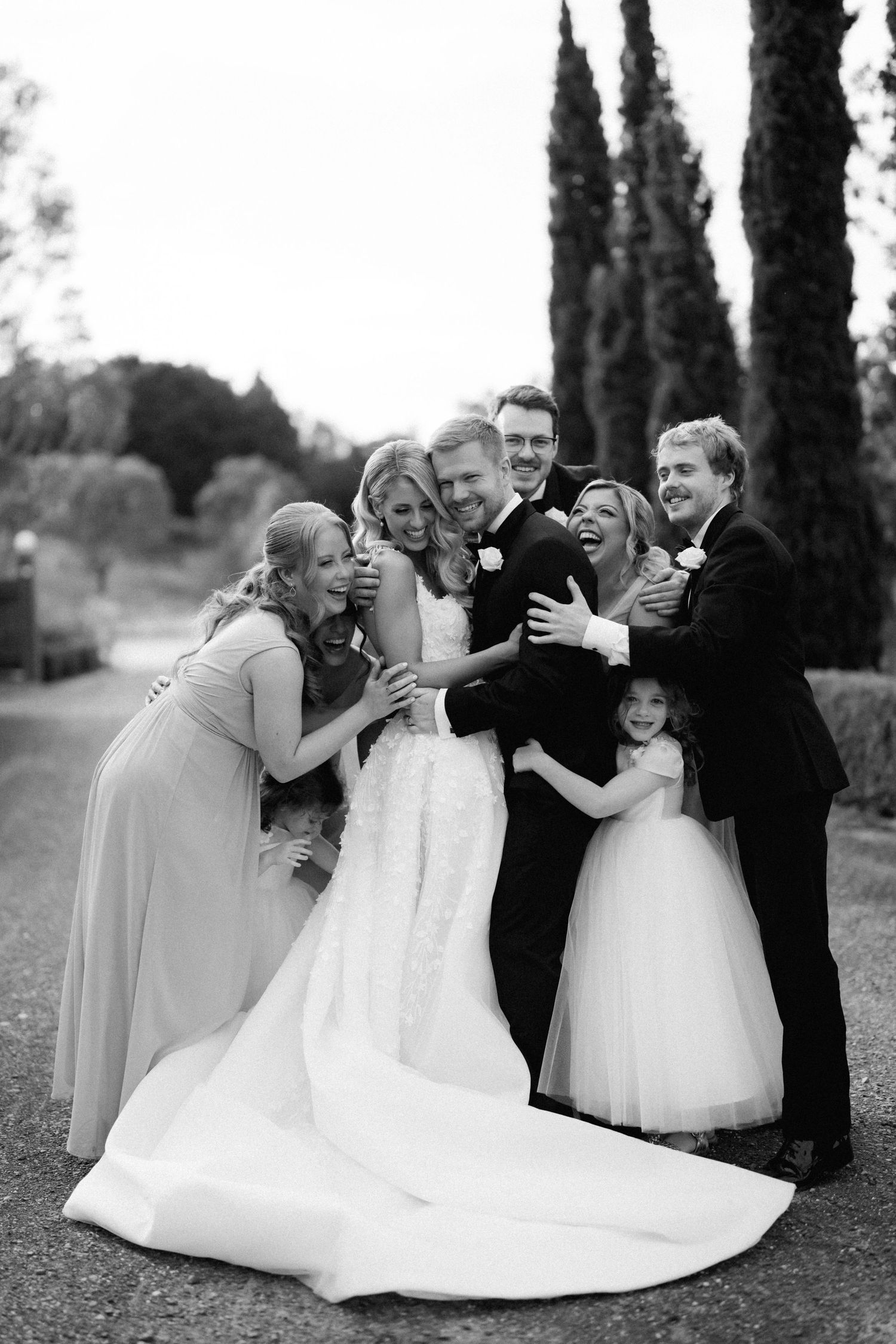 Candid black and white photo of wedding party sharing laughter and embraces.