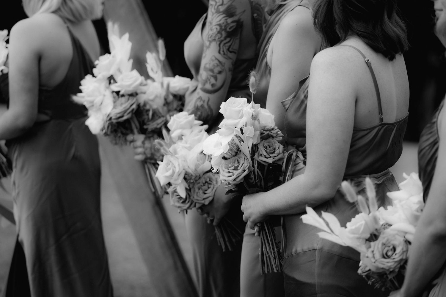 Black and white photo of bridesmaids holding elegant white floral bouquets during a wedding ceremony.