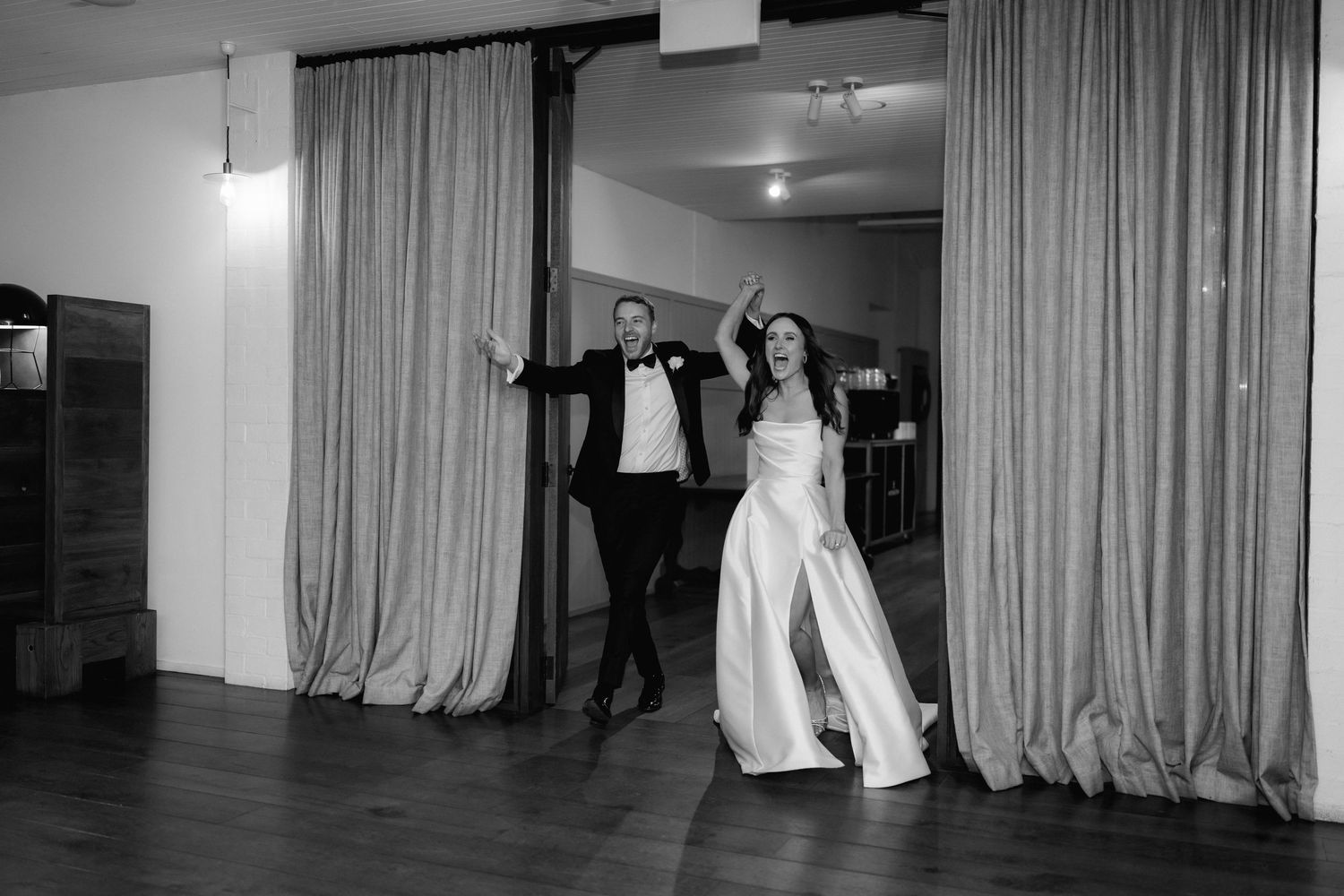 A couple dances joyfully in front of floor-length curtains during their wedding celebration.