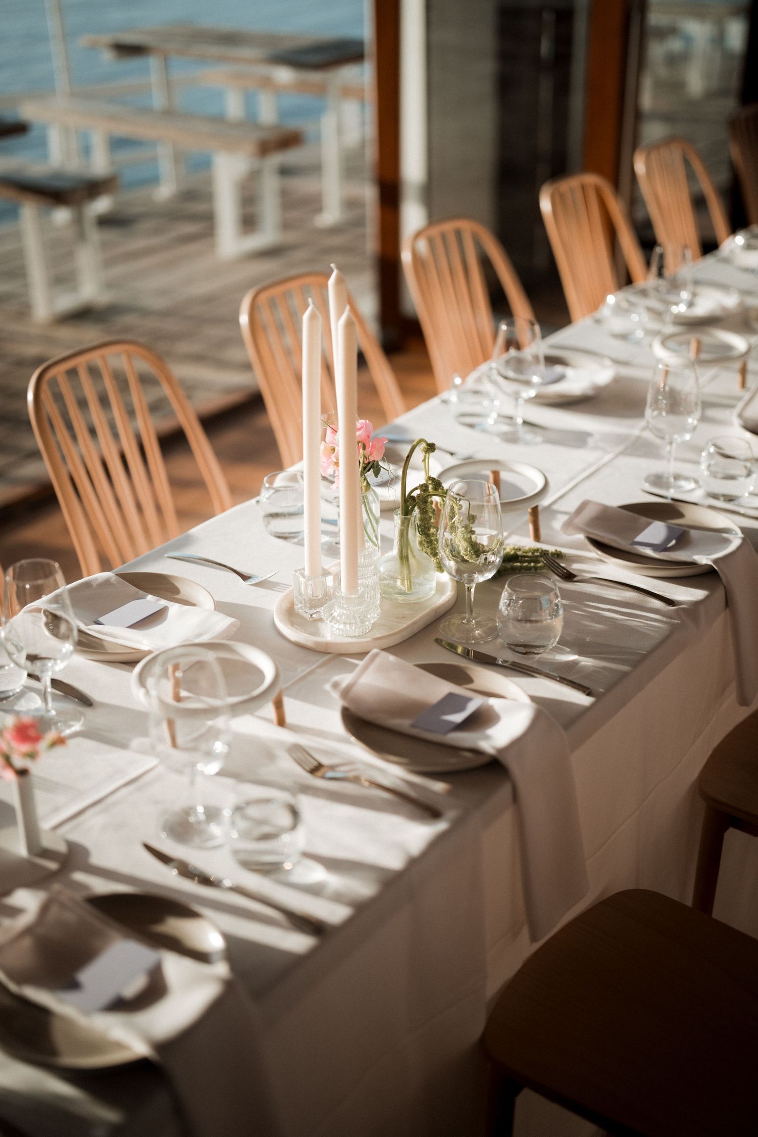 Formal dining table set with white linens, candles and wooden chairs for an elegant wedding reception.