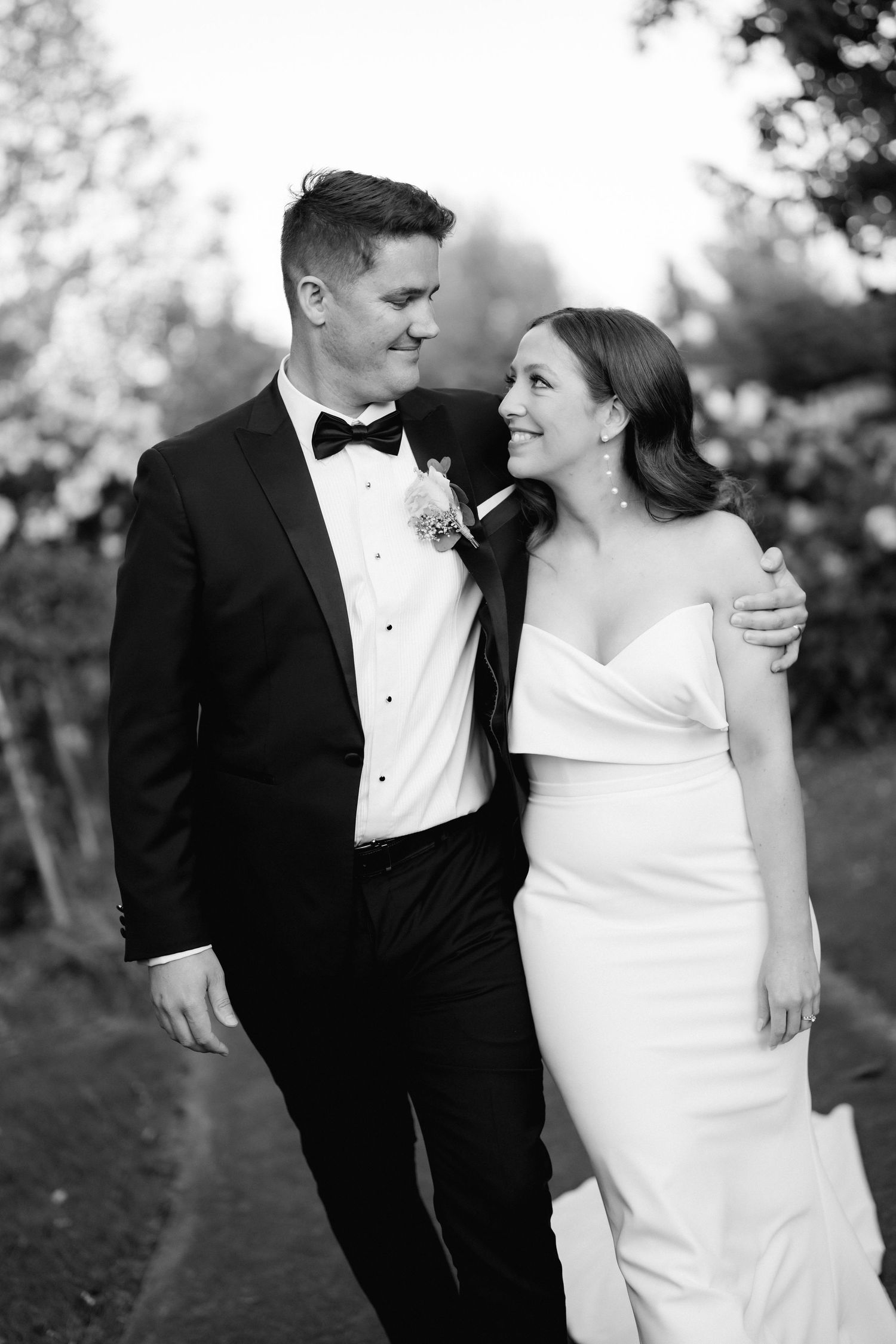 Elegant wedding couple shares intimate moments in formal attire outdoors with black tux and white gown.