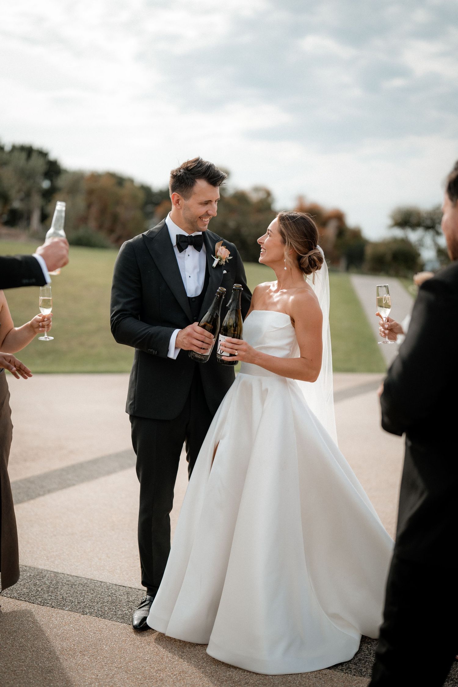 Newlywed couple shares a moment and champagne toast during outdoor wedding celebration at sunset.