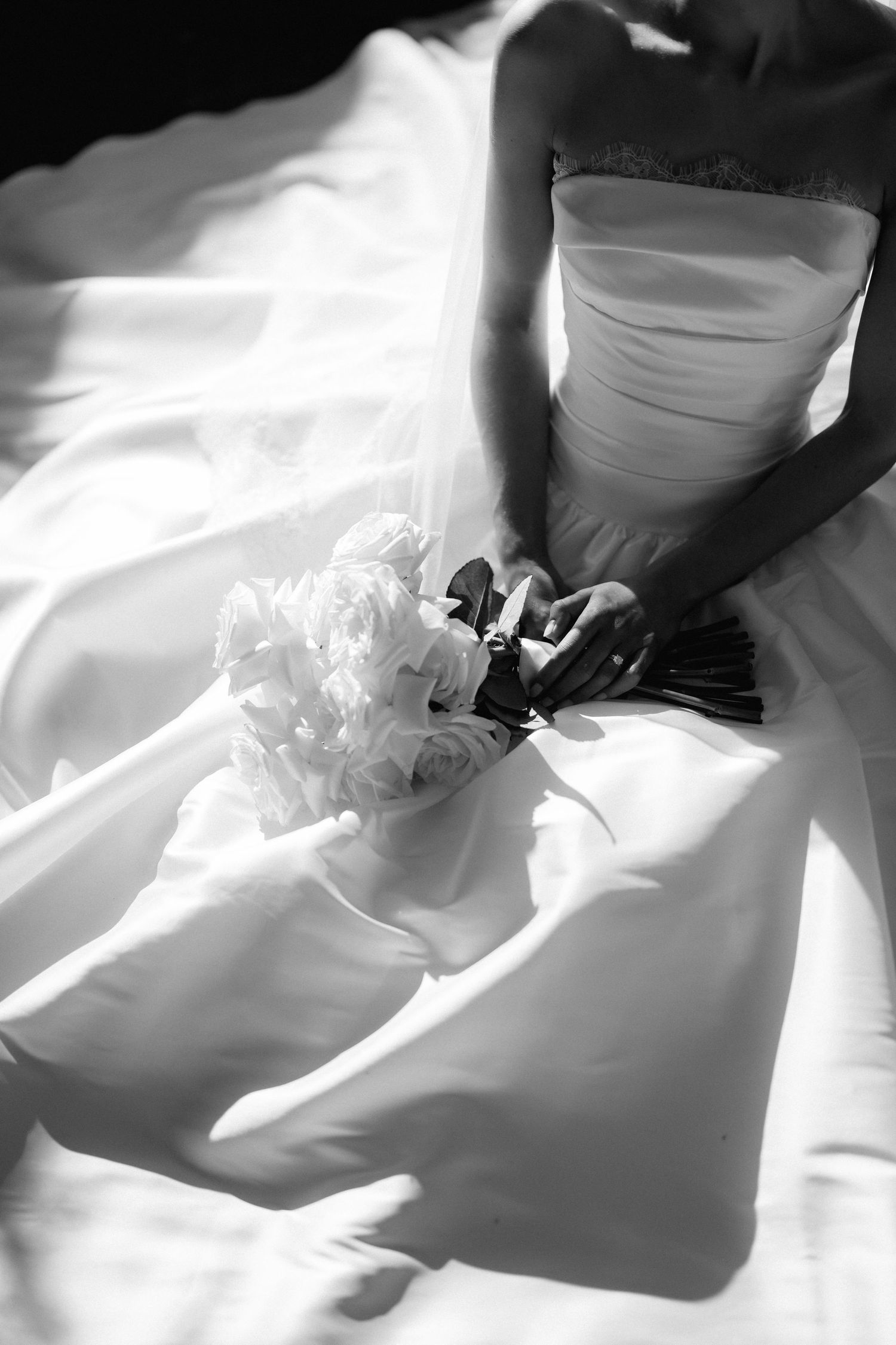 Black and white detail of wedding dress with roses in dramatic lighting.