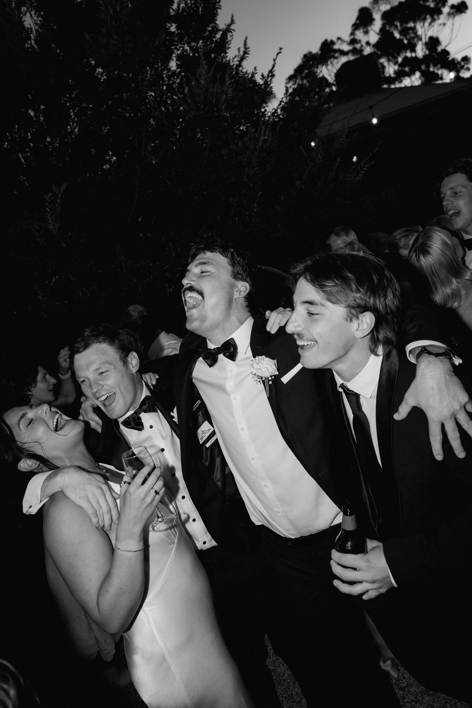 A black and white photo showing a group laughing and enjoying a candid moment at a formal event.