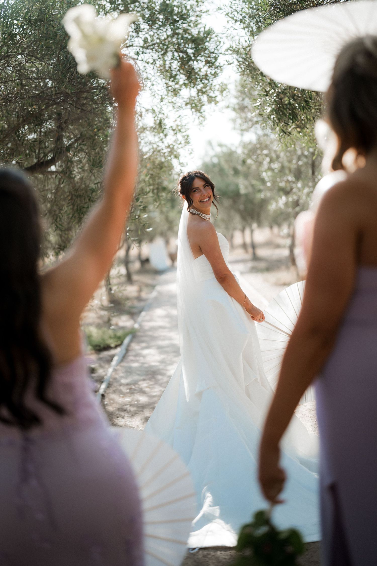 Bride twirls in white wedding dress outdoors while others watch.