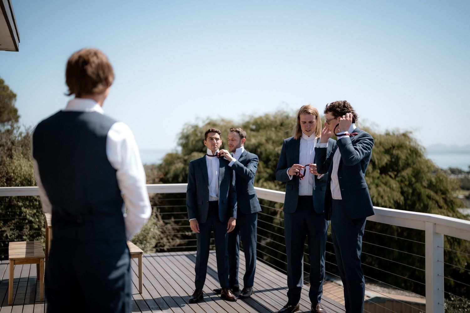 A group gathers on an outdoor deck overlooking trees and distant scenery on a sunny day.