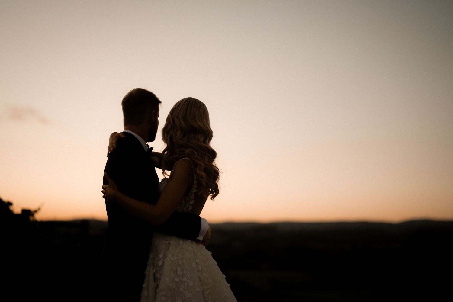 Silhouetted bride and groom share an intimate moment against a warm sunset sky.