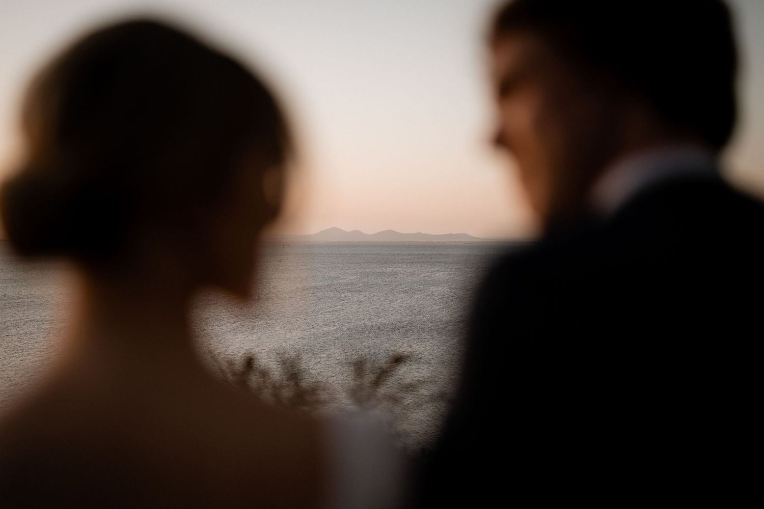 A silhouetted couple stands close together against a dusky sunset backdrop.