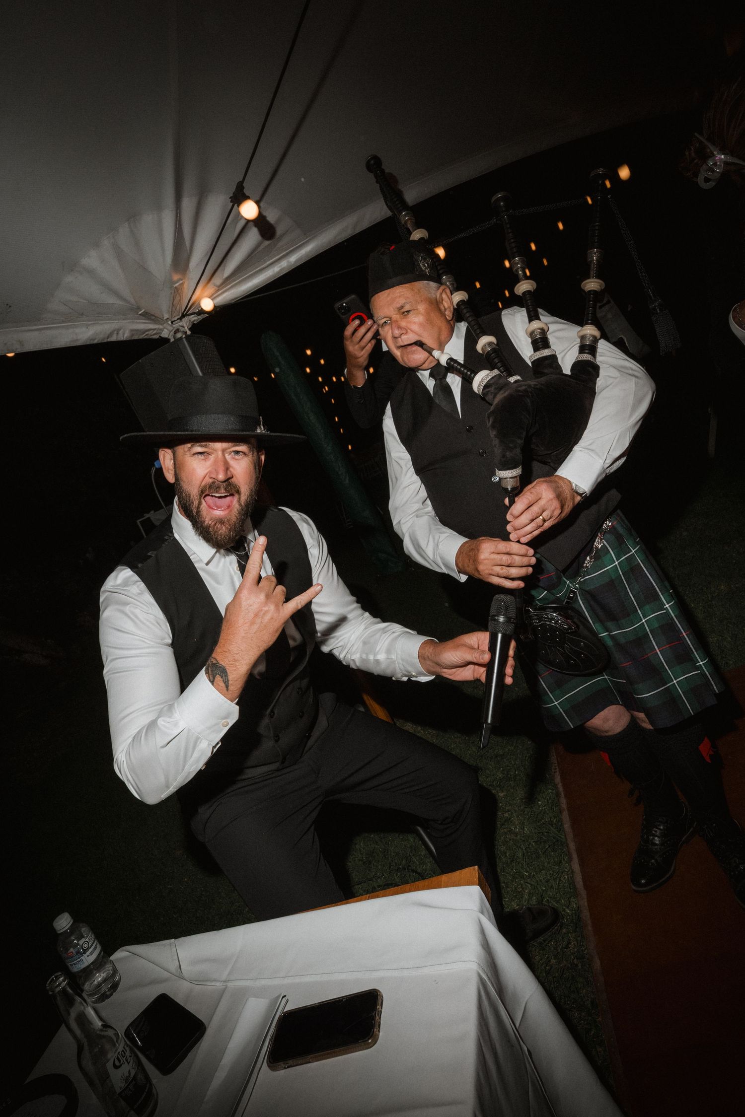 Bagpipers in traditional Scottish attire perform energetically at nighttime wedding celebration.