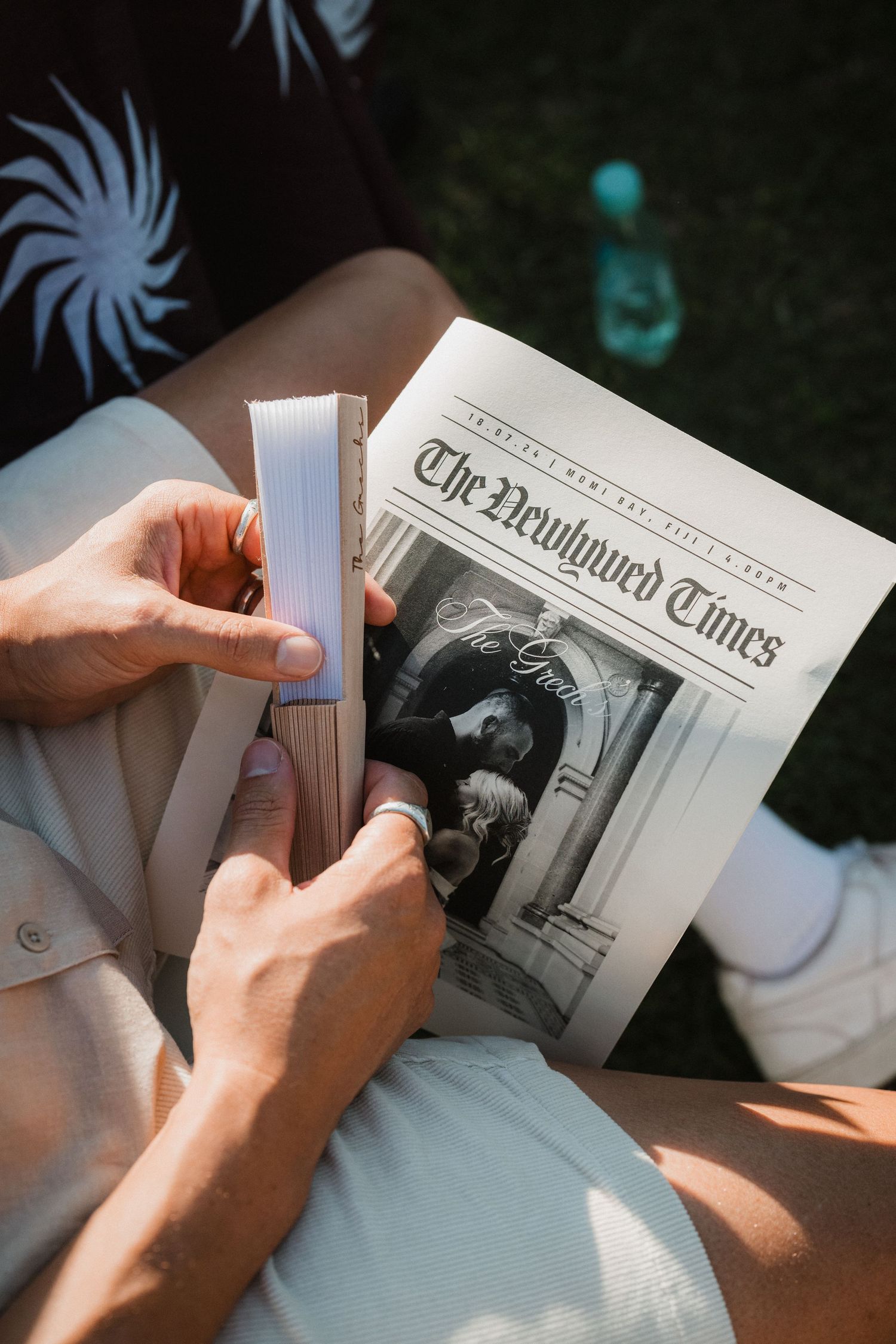 Hands holding and reading a newspaper during an outdoor event.