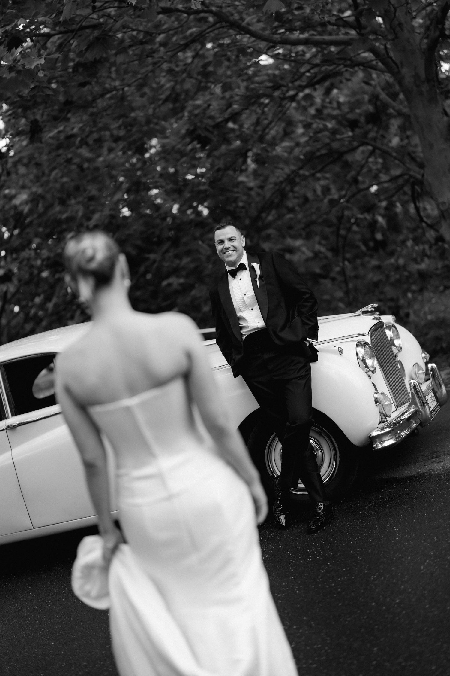 Artistic black and white photo captures wedding couple with vintage car.