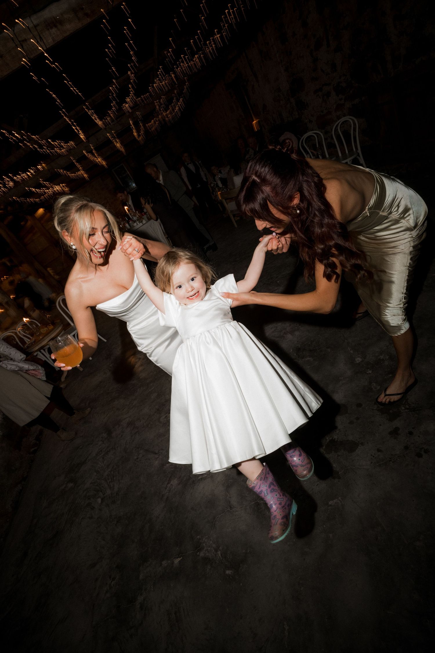Wedding guests dance and celebrate on a dark dance floor at the reception.