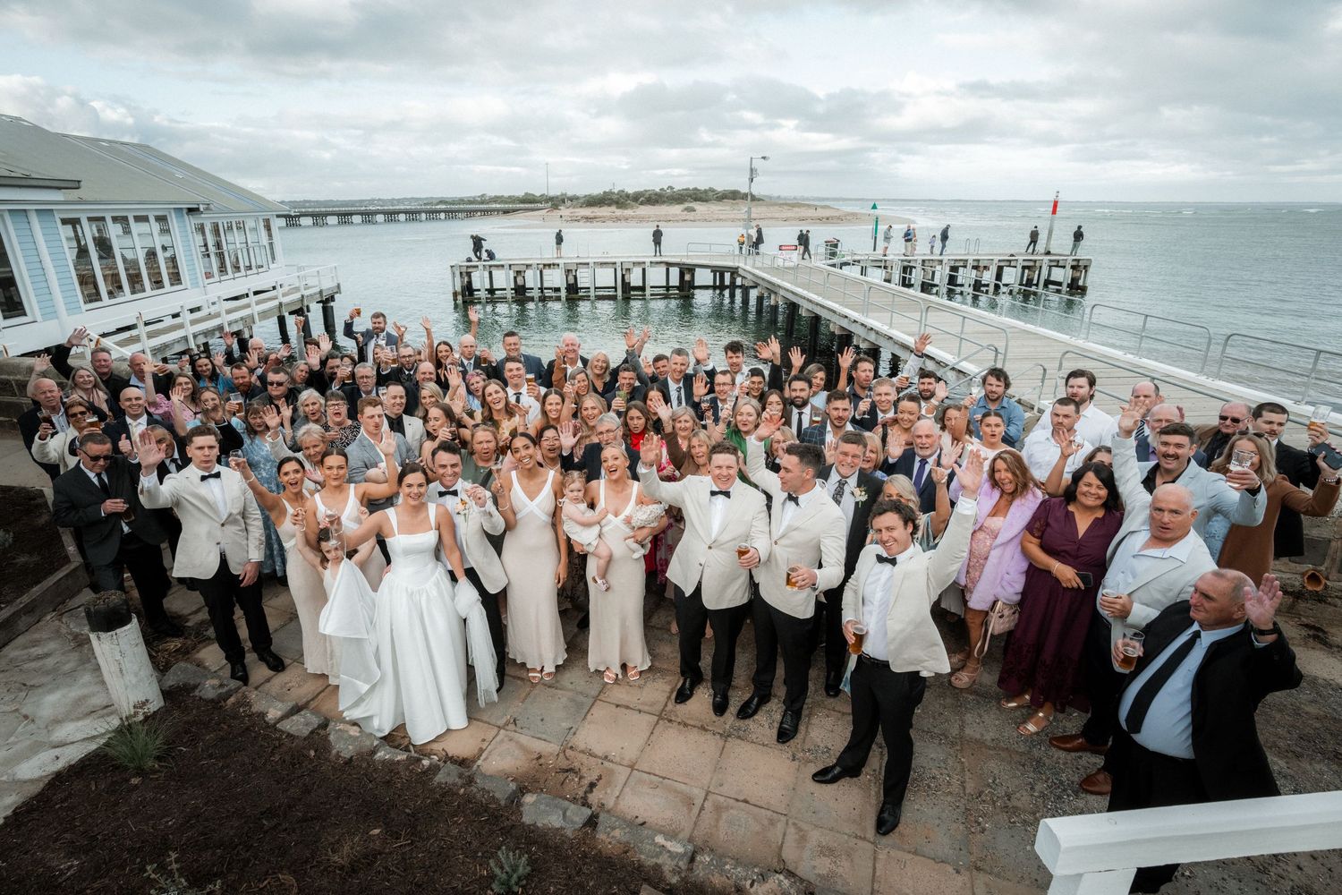 Wedding party and guests gathered on an oceanfront pier during sunset celebration at coastal venue.