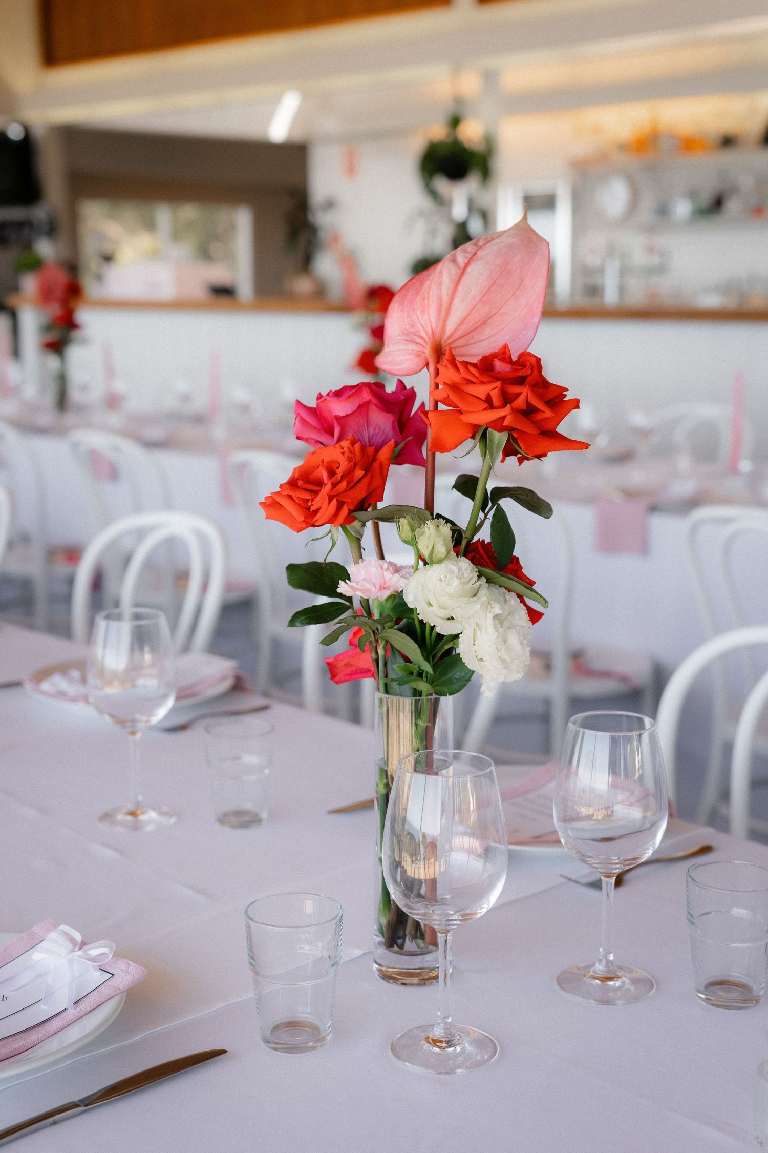 Elegant wedding reception table with colorful floral centerpiece featuring pink, red, and white roses in a glass vase.