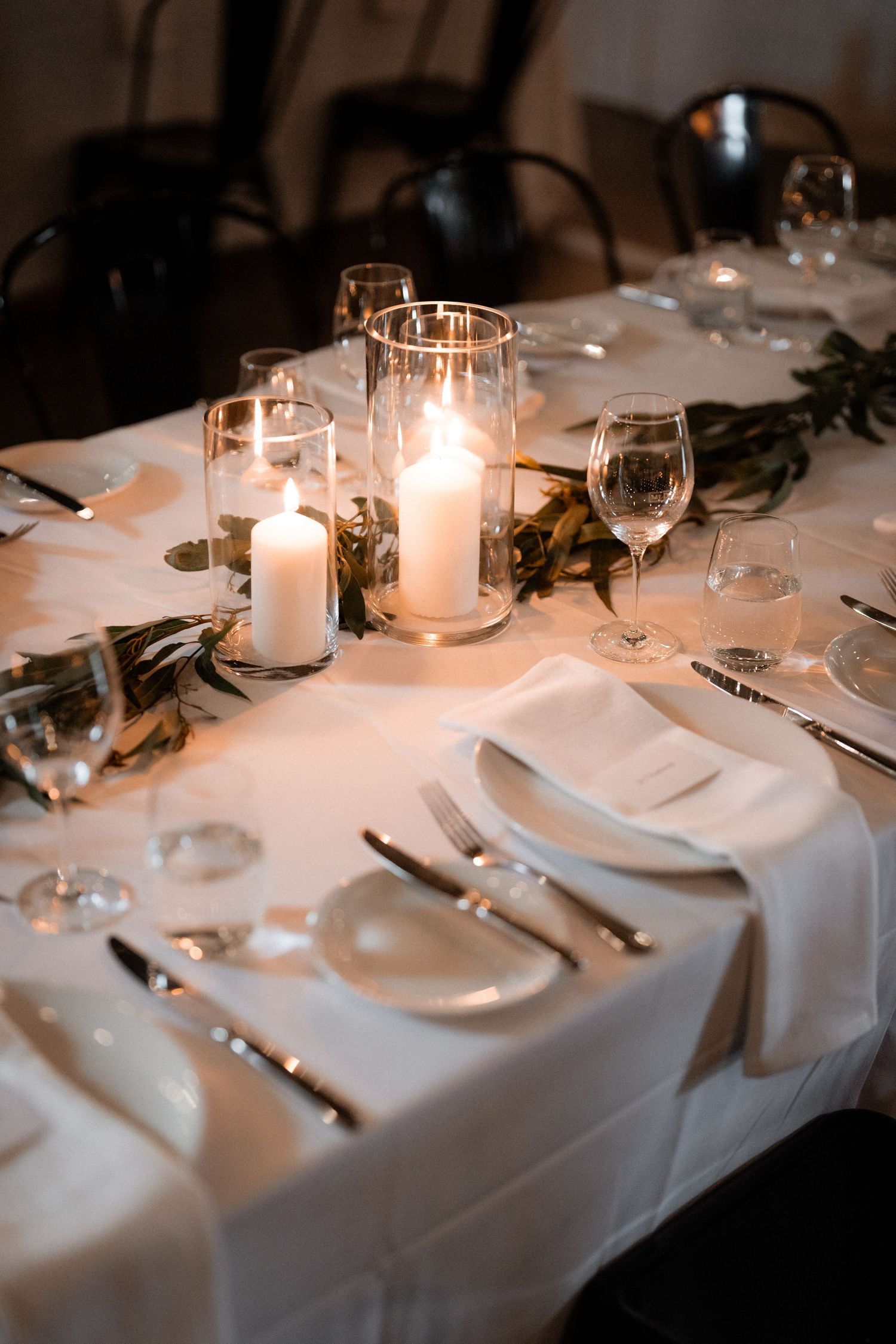 Romantic wedding table setting with glowing candles, wine glasses, and white linens.