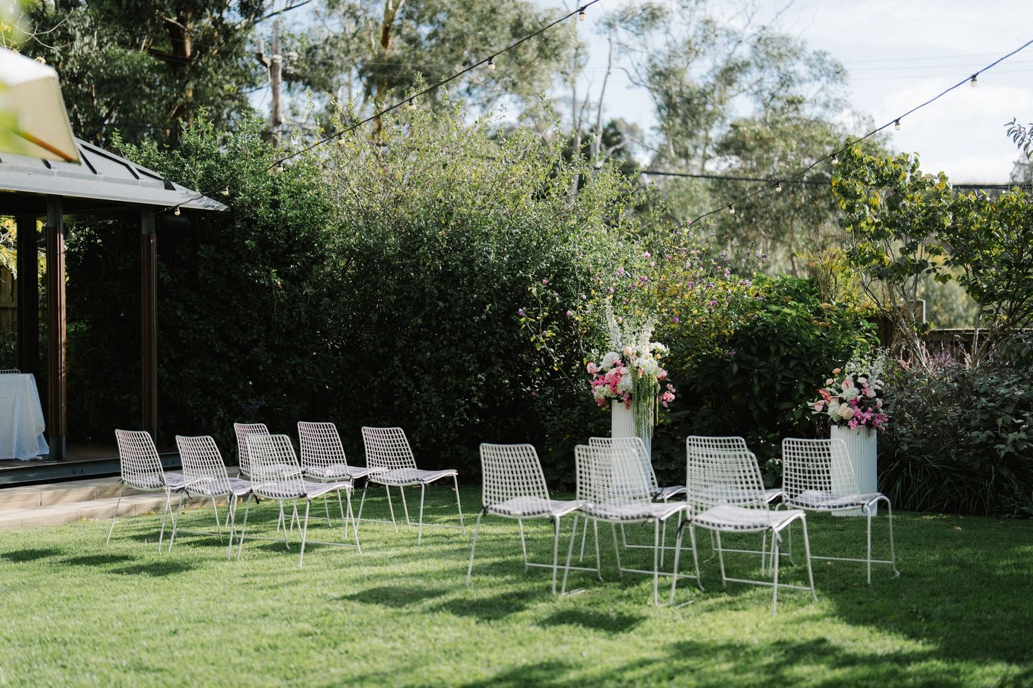 White outdoor chairs arranged on a lush green lawn for an elegant garden event setup.