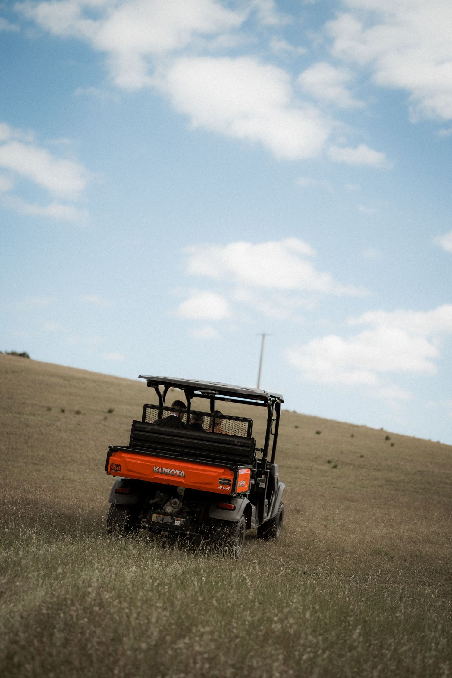 An orange utility vehicle sits on a grassy hillside against a bright blue sky.