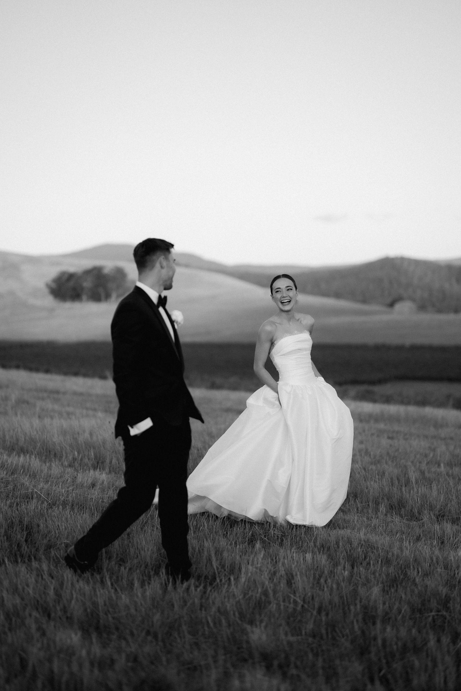 A couple poses in a field at sunset creating dramatic black and white silhouettes against rolling hills.