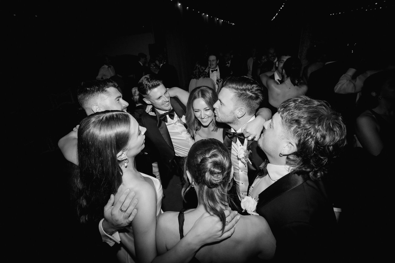Party guests dancing and celebrating at a lively wedding reception in dark lighting.