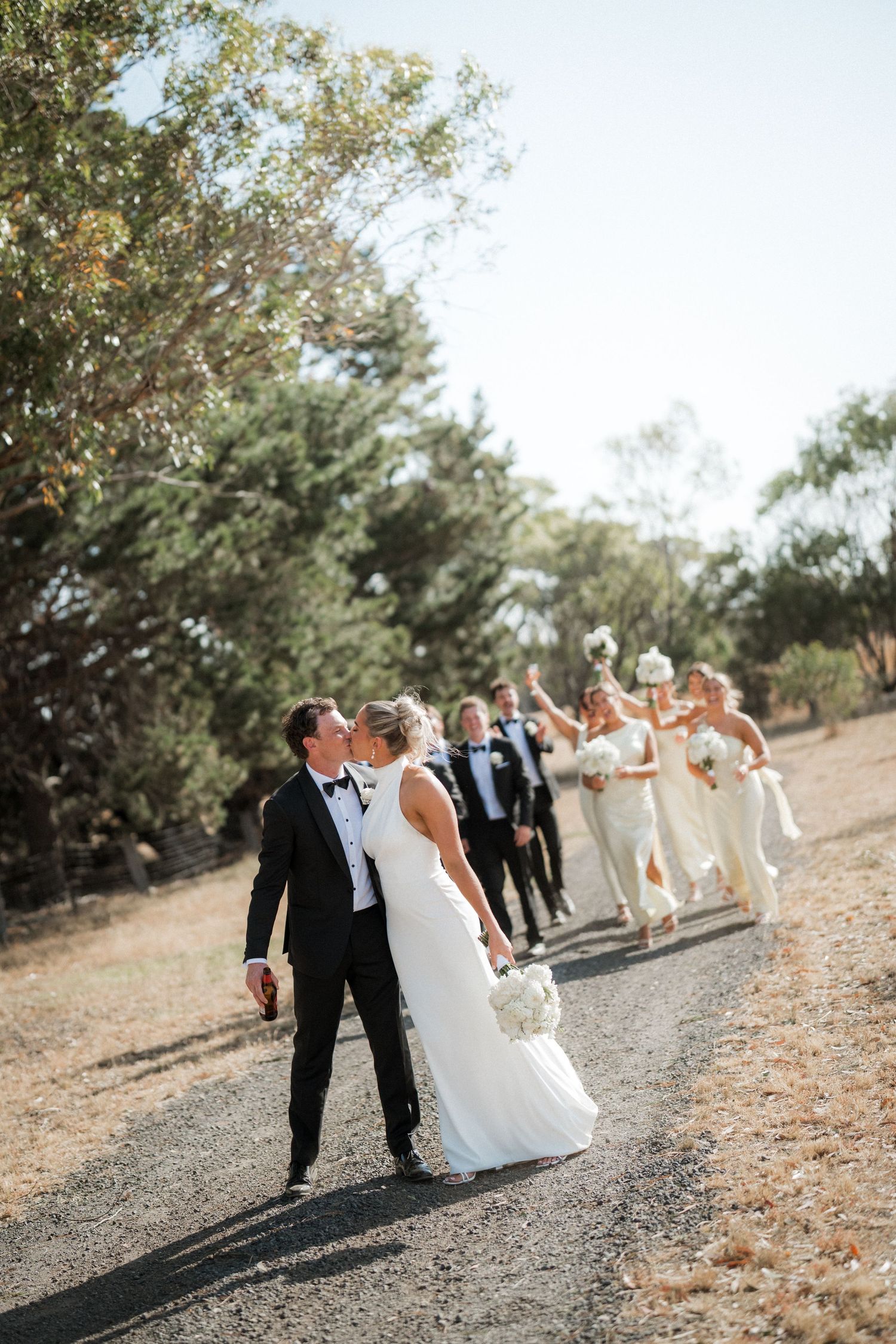 A wedding party walks along a scenic dirt path surrounded by trees and natural landscape.