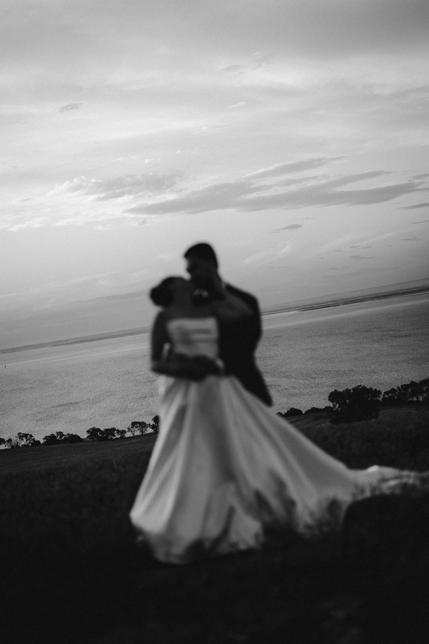 Silhouetted couple dancing at sunset with bride's dress flowing dramatically in black and white.
