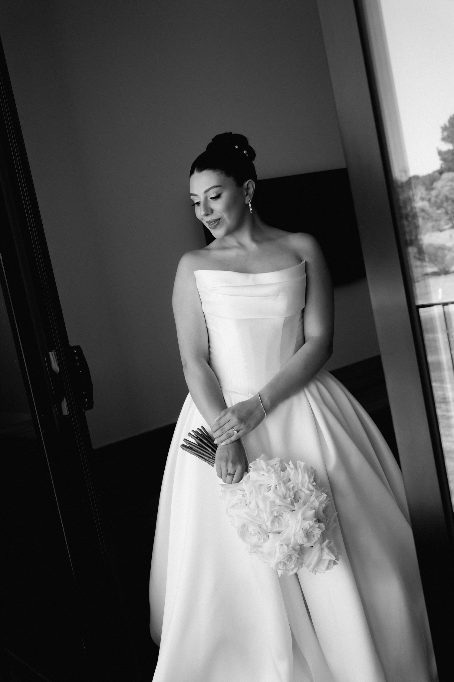 A classic black and white bridal portrait shows an elegant strapless ballgown wedding dress with a white bouquet.