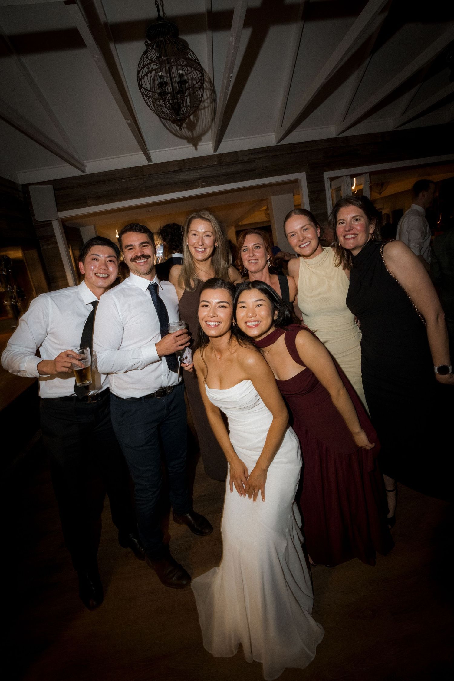 Bride in white strapless gown posing with wedding guests on the dance floor at reception.