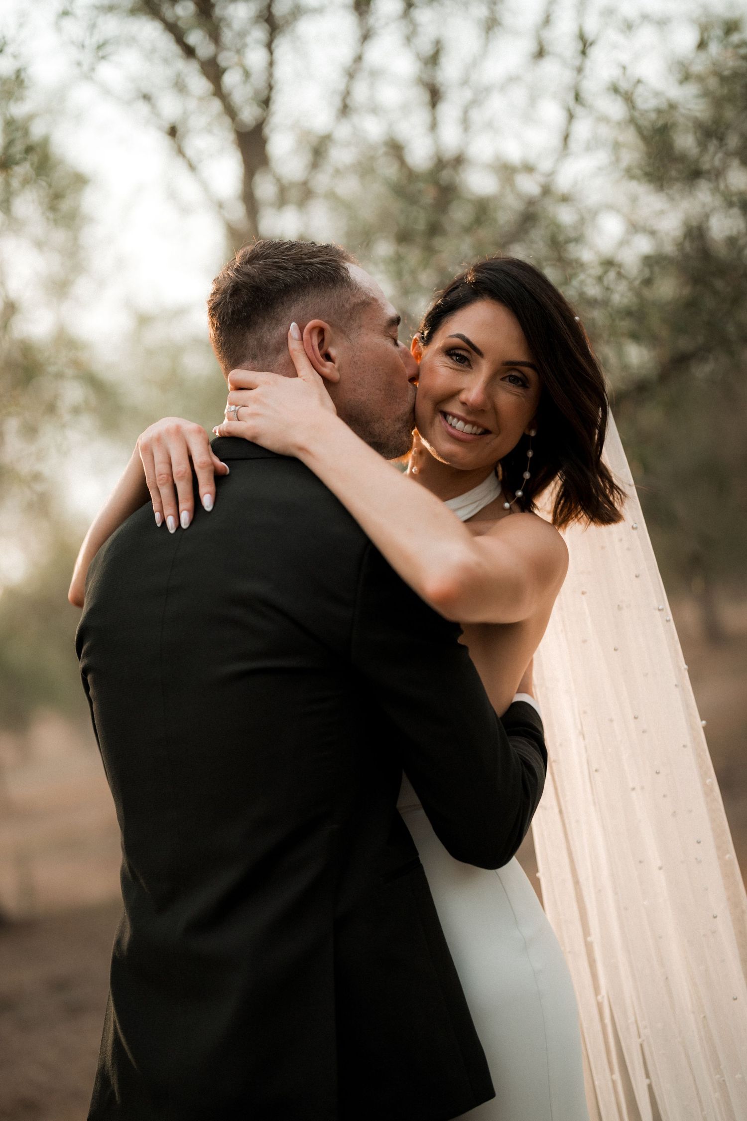 A couple shares an intimate embrace during their sunset wedding photoshoot in a rustic outdoor setting.