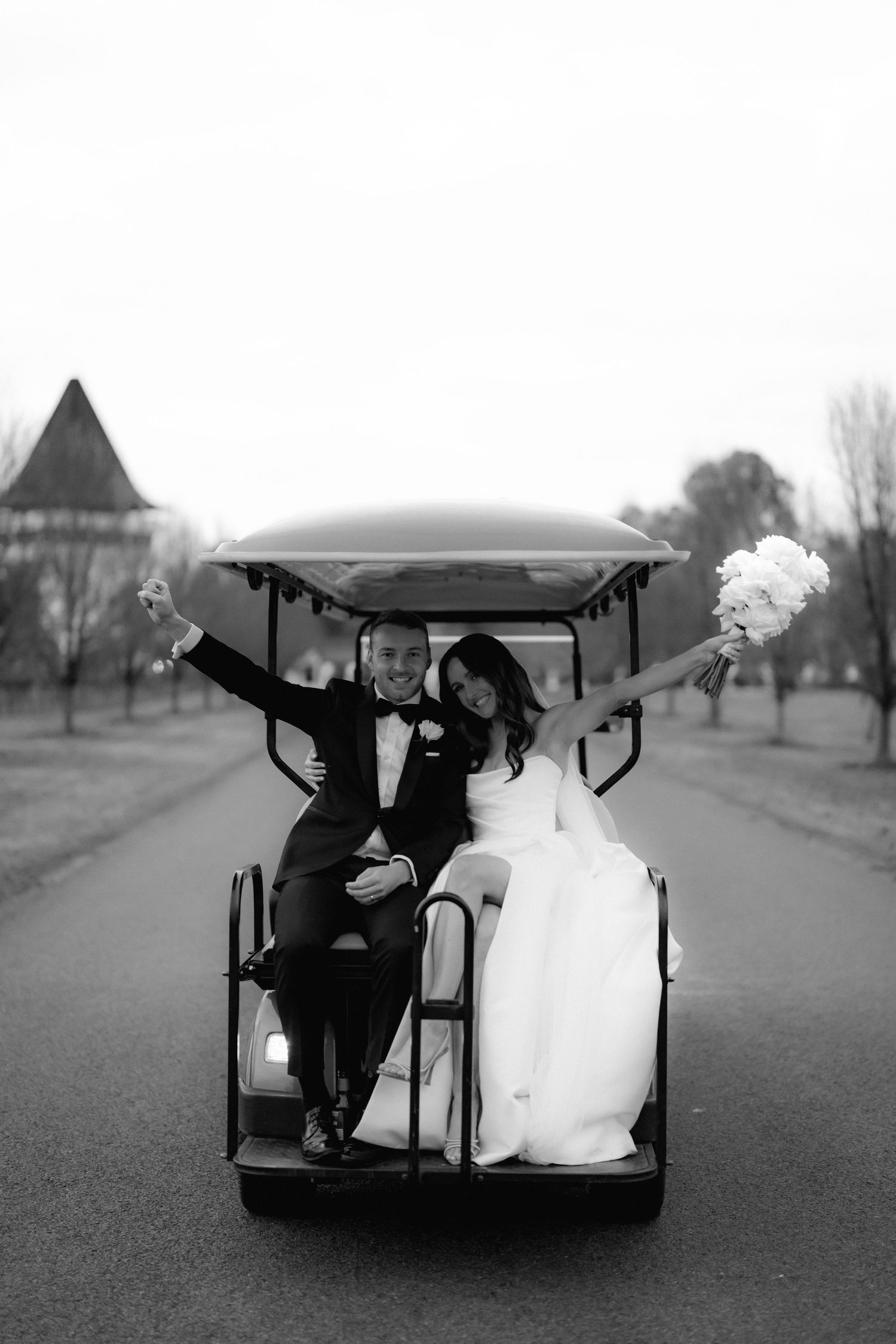 Newlyweds ride in a golf cart while holding white flowers on their wedding day.