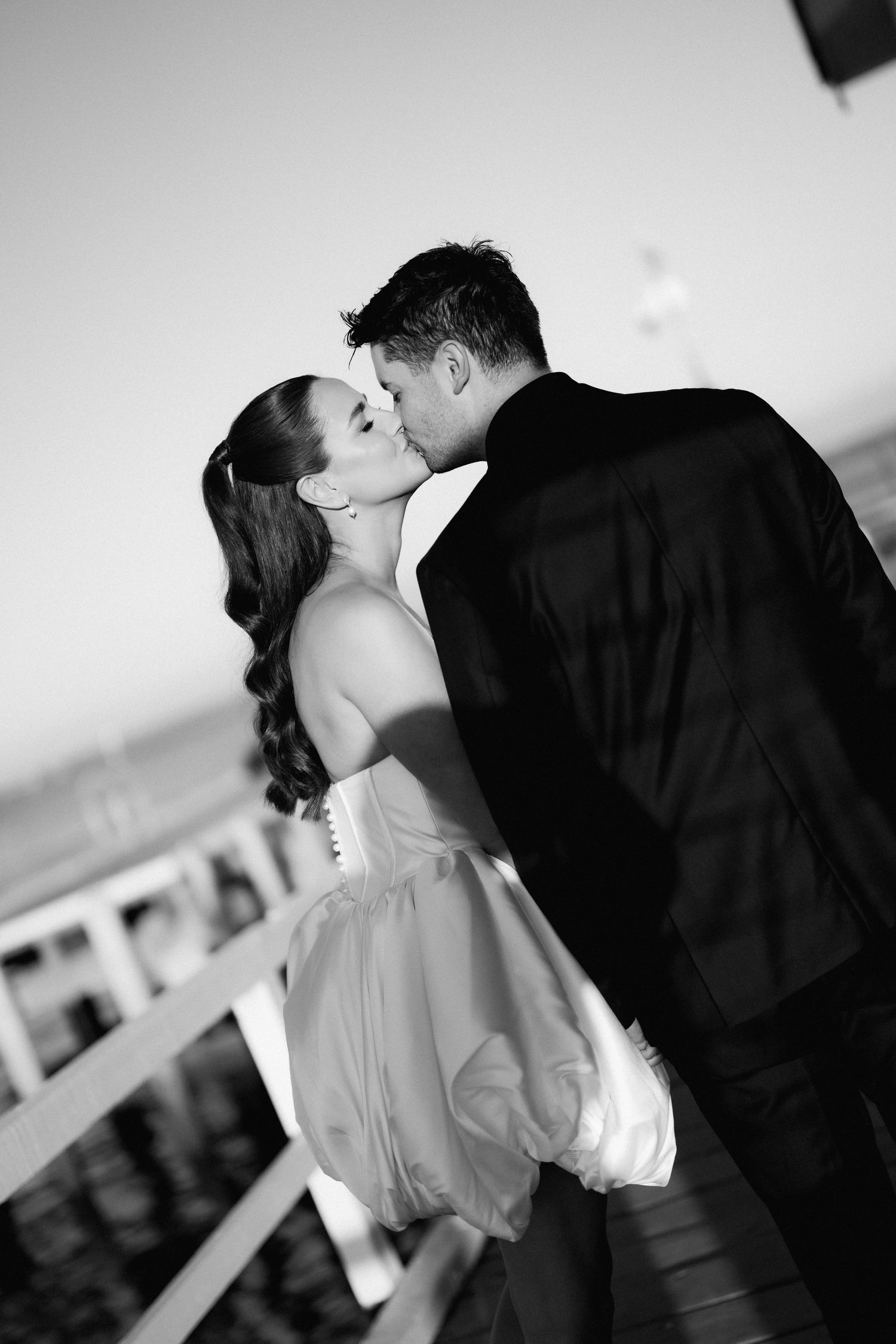 A romantic black and white wedding photo capturing a couple kissing on a balcony.