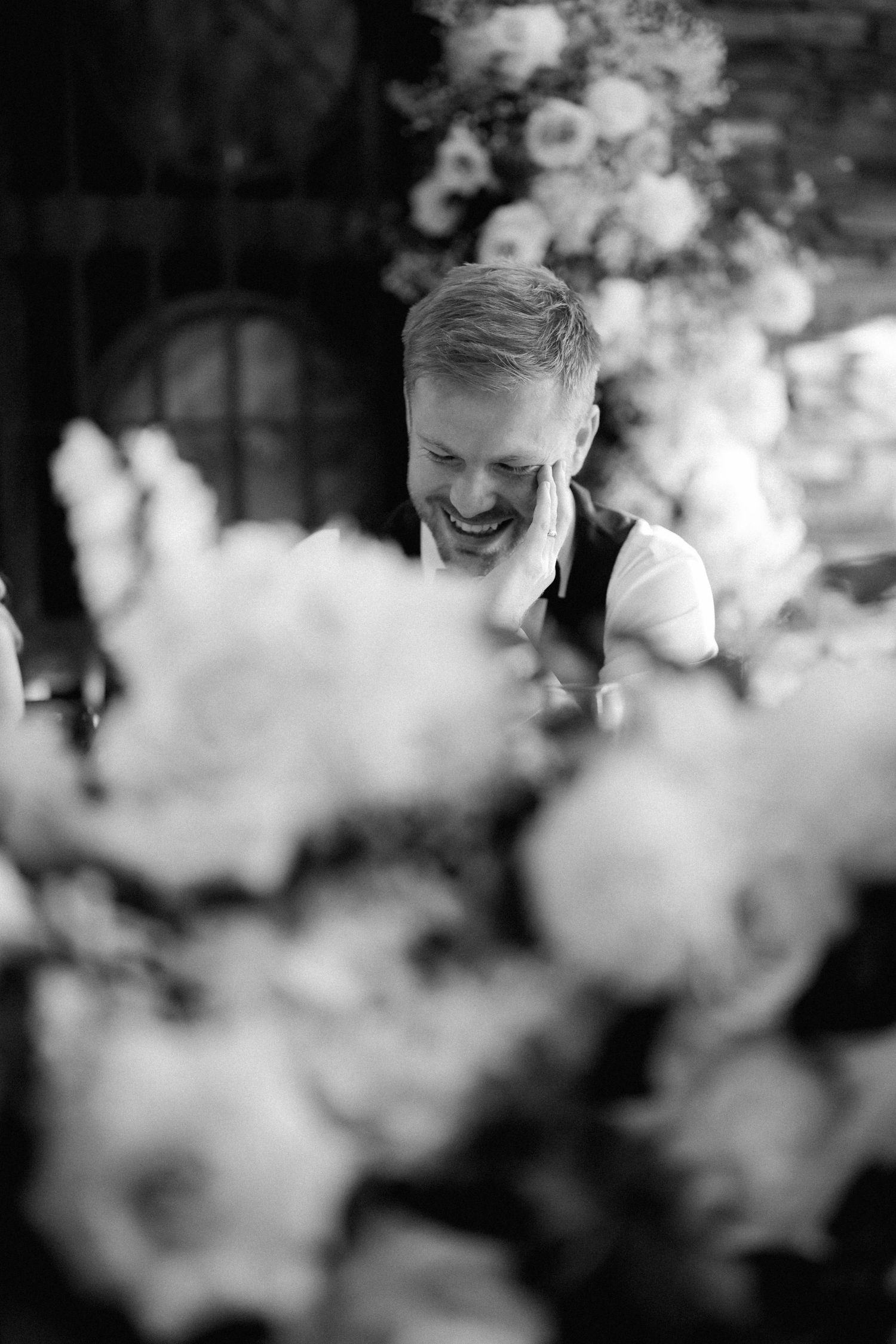 Black and white candid photo through flowers showing genuine laughter and joy.