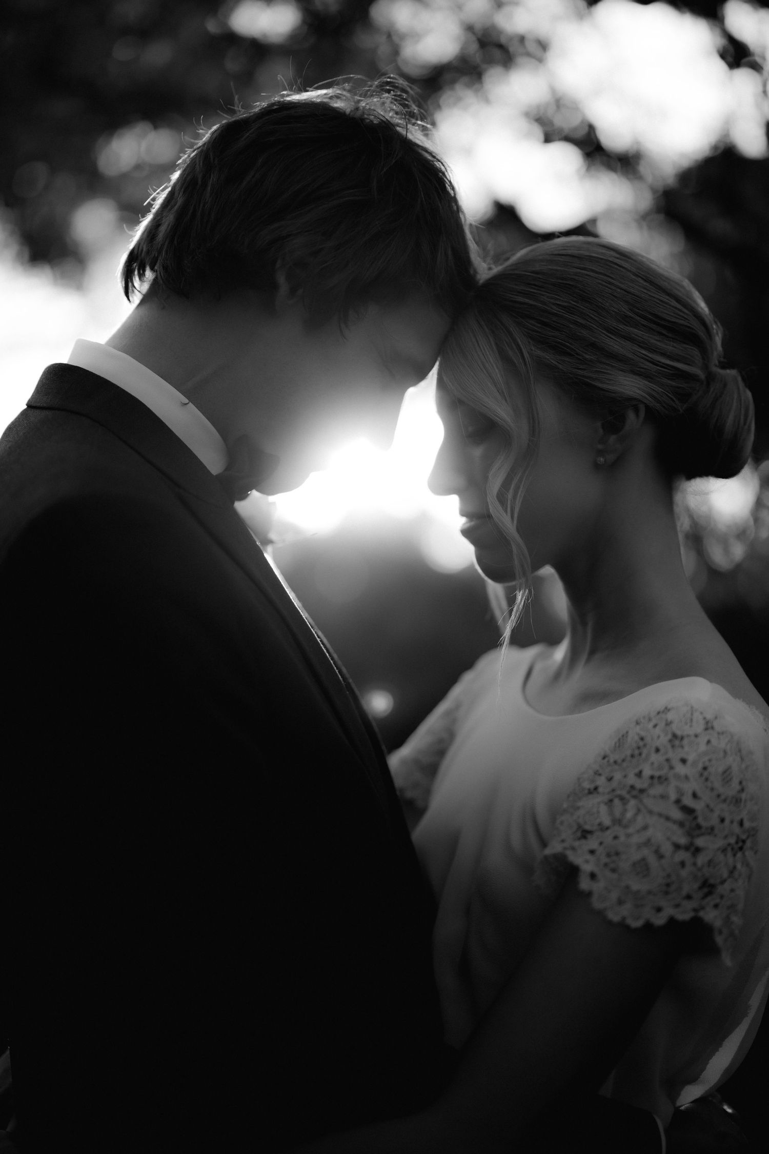 A romantic black and white silhouette of a bride and groom sharing an intimate moment in soft sunlight.