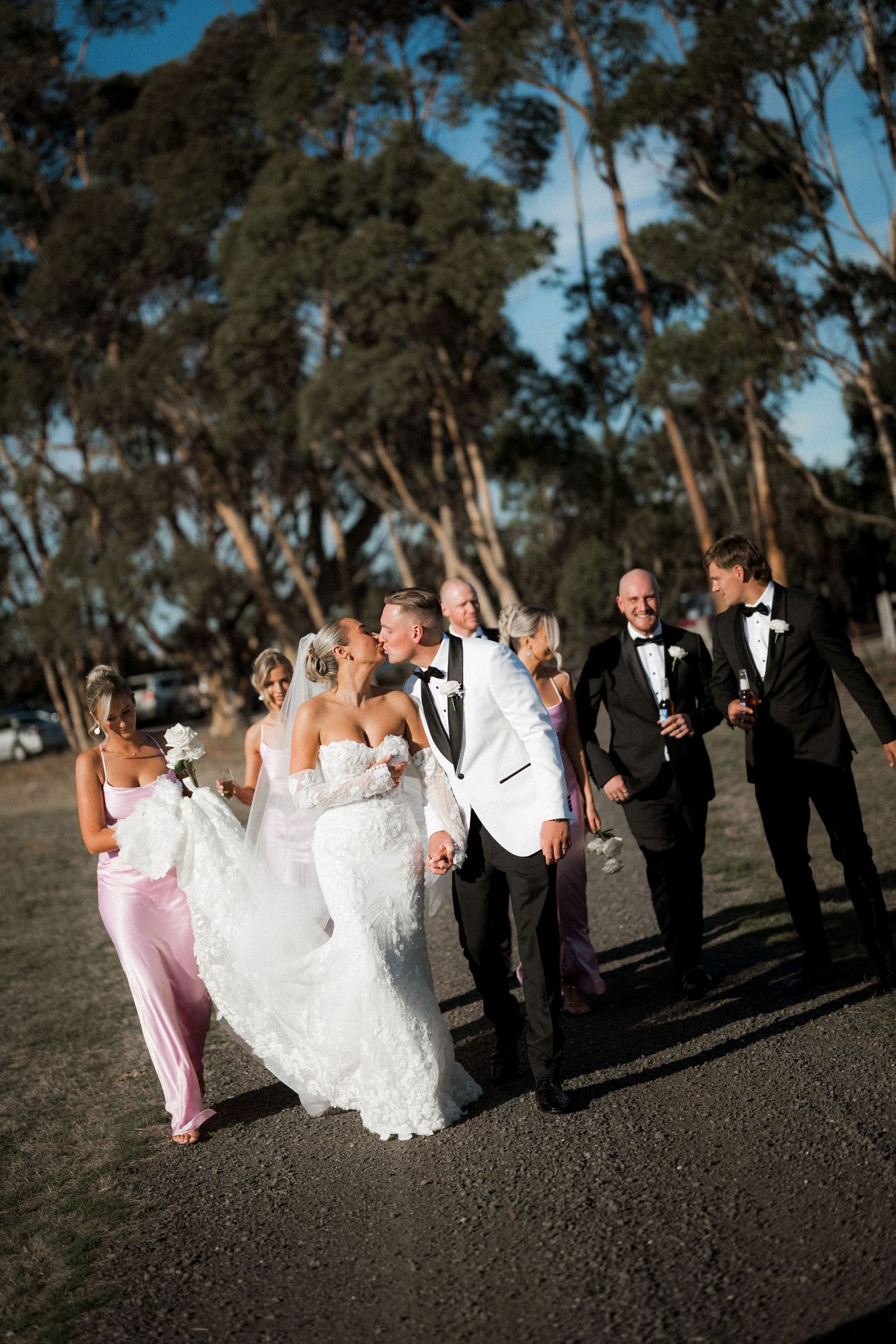 Wedding party in formal attire walks together on a path with tall eucalyptus trees in the background.