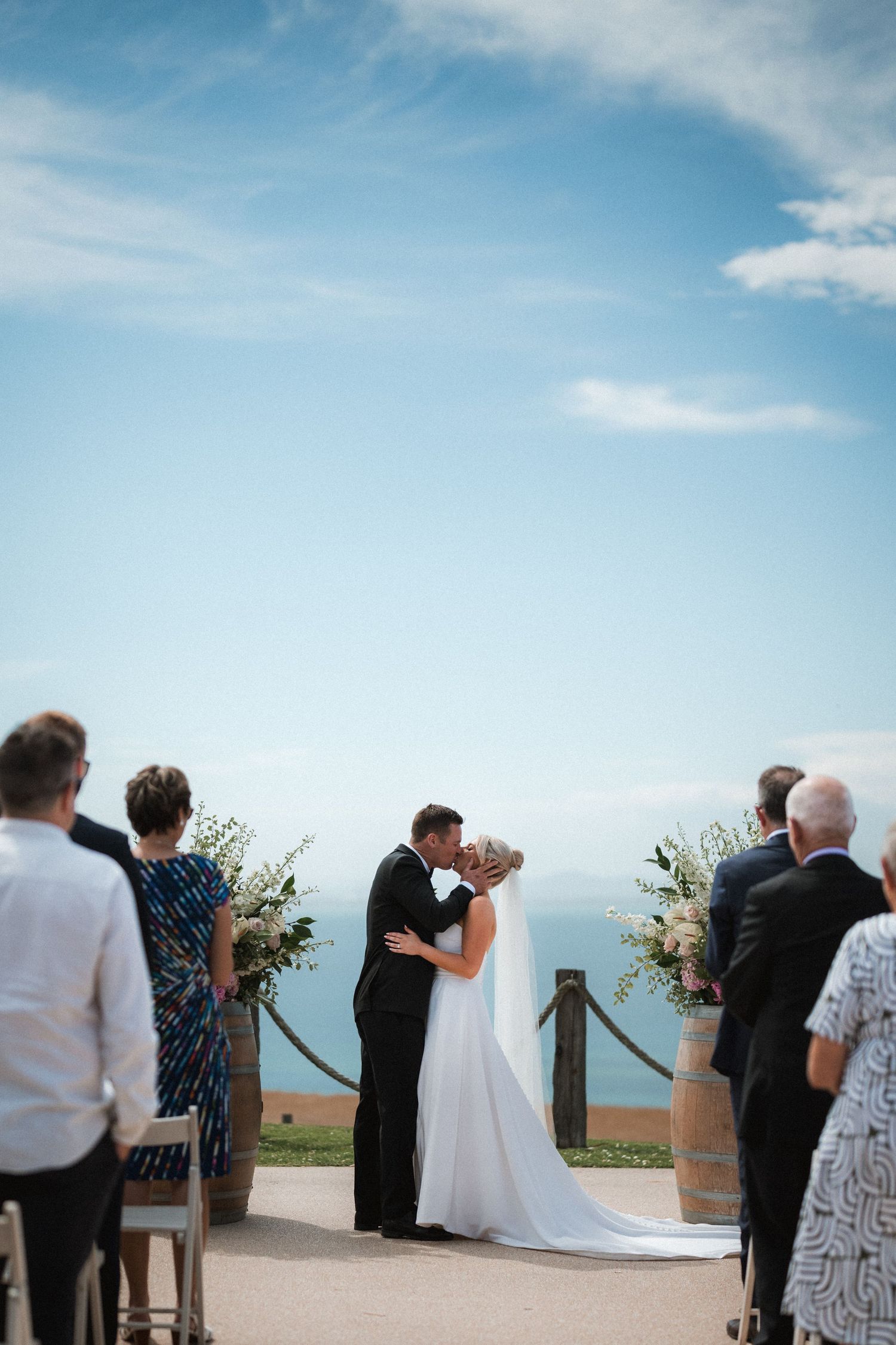 Intimate outdoor wedding ceremony overlooking the ocean with wine barrel floral arrangements.