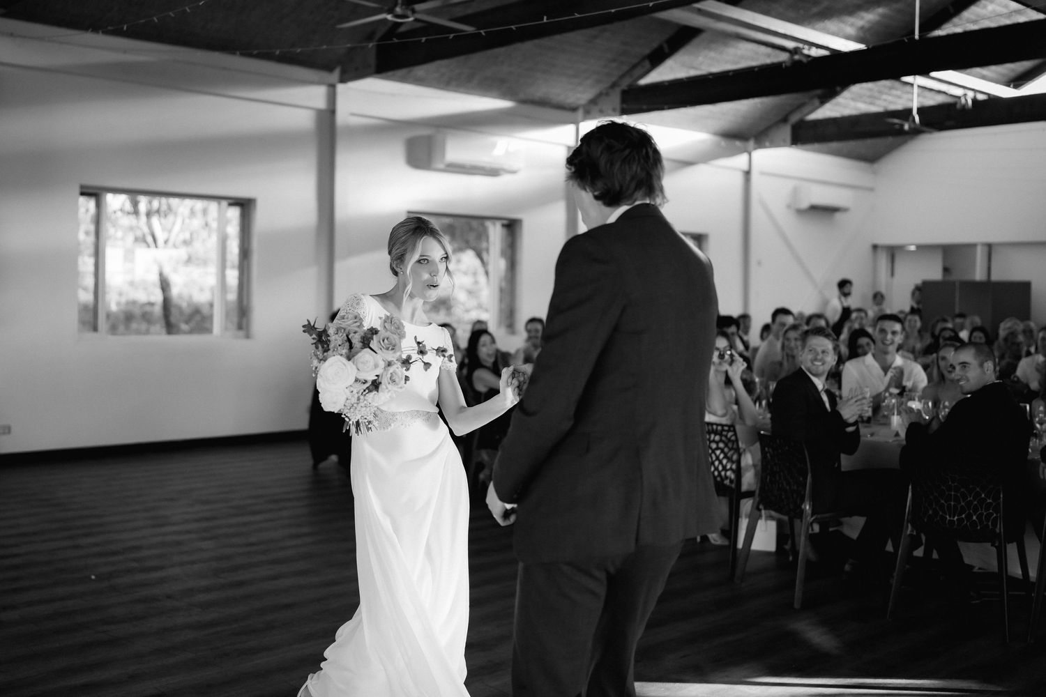 Black and white photo of a couple sharing their first dance at a wedding reception.